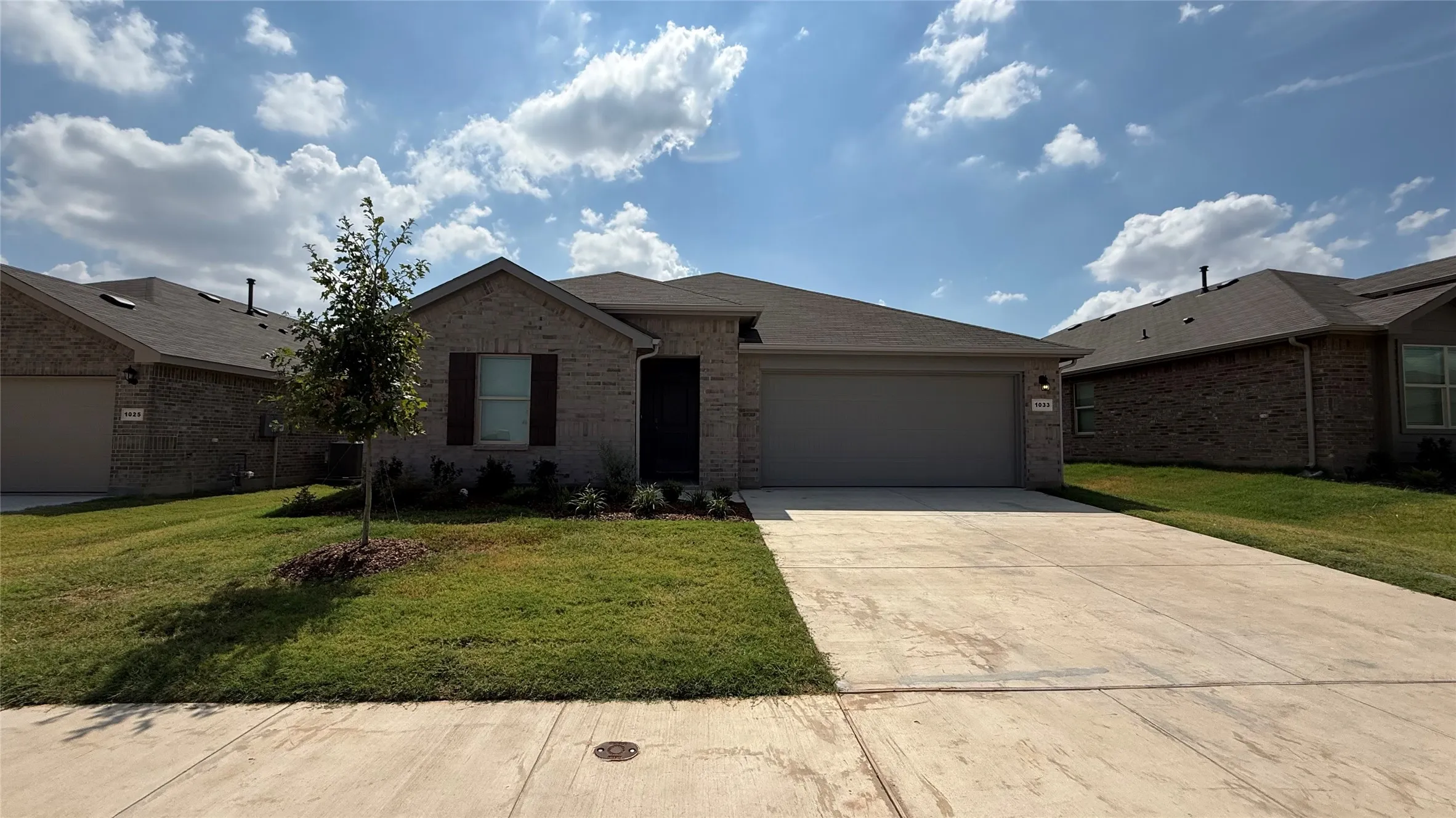 Brick exterior with a gray garage door, concrete driveway, and a manicured lawn