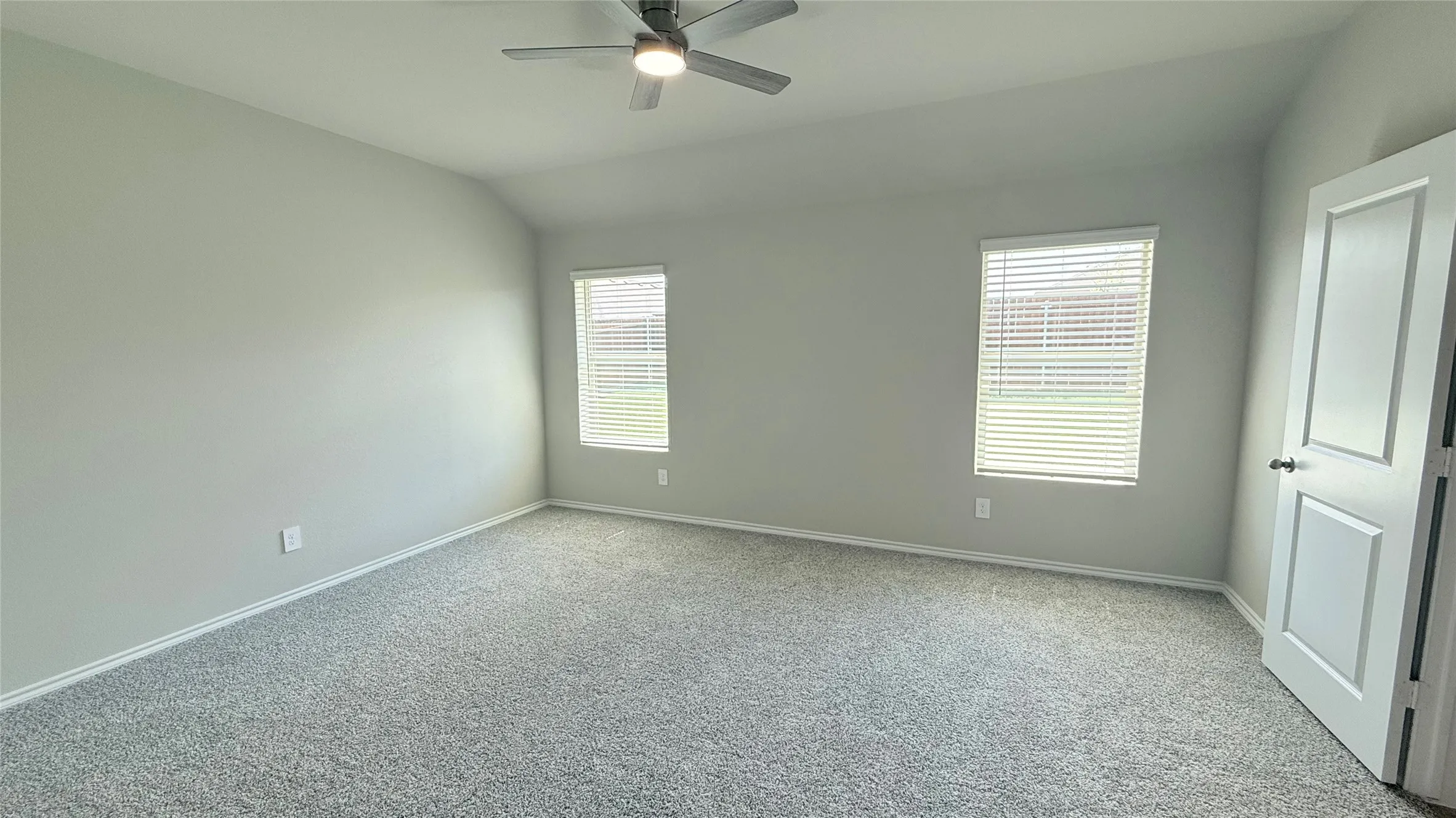 Vaulted ceiling bedroom with neutral wall tones and plush gray carpeting