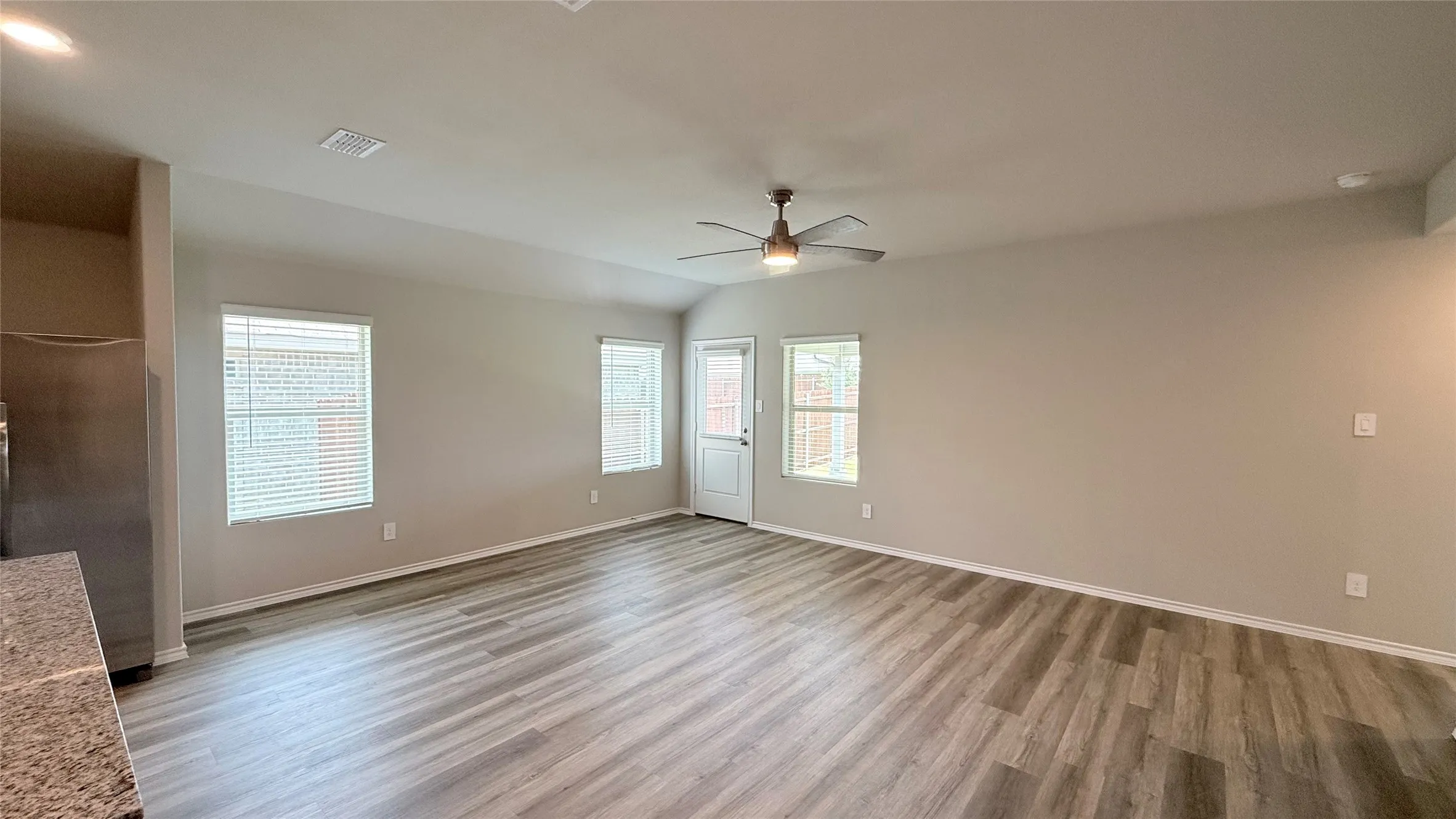 Spacious interior featuring wood-finish flooring, a ceiling fan, and multiple windows