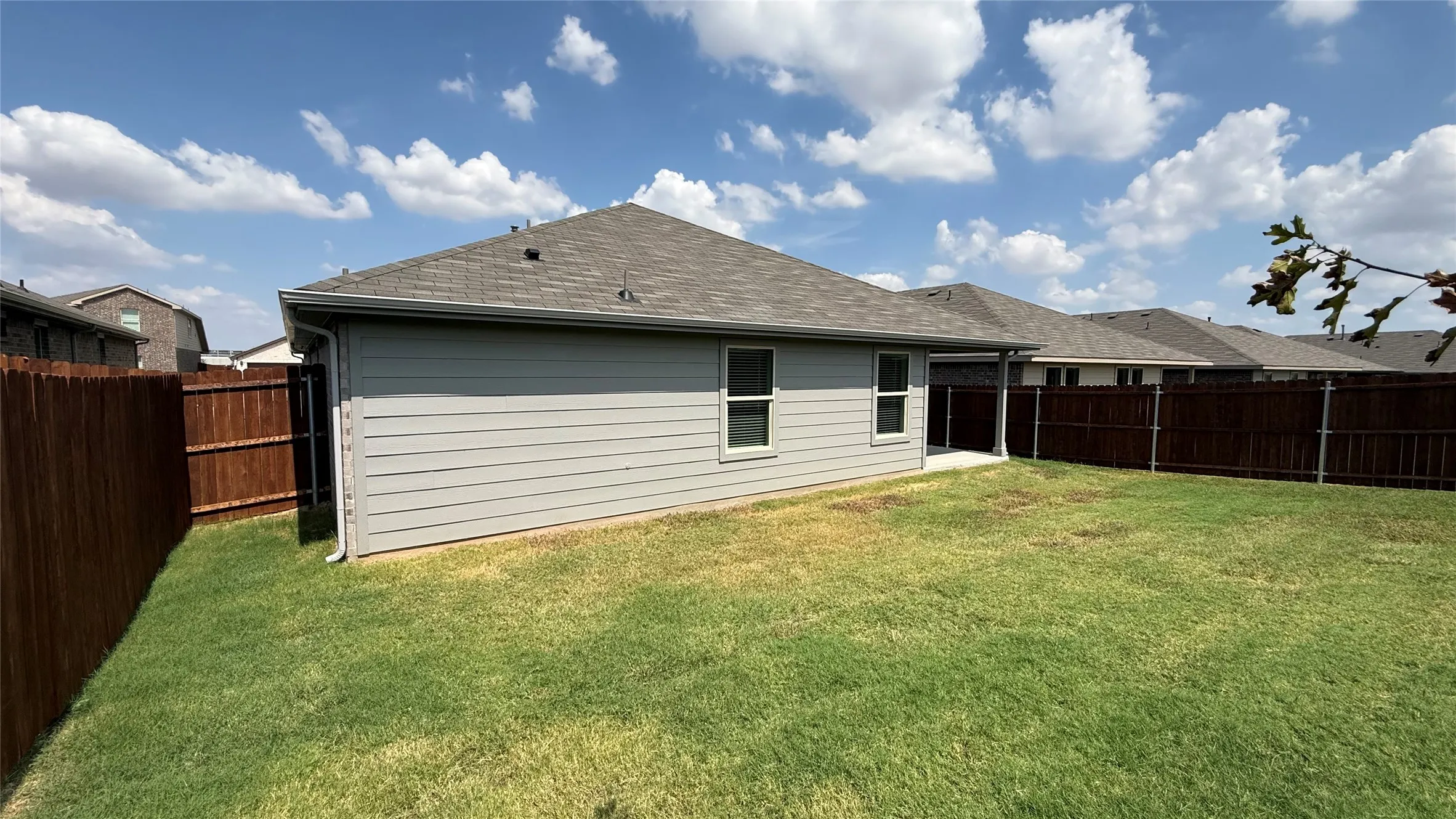 Expansive backyard featuring a manicured lawn, full privacy fencing, and a covered patio area