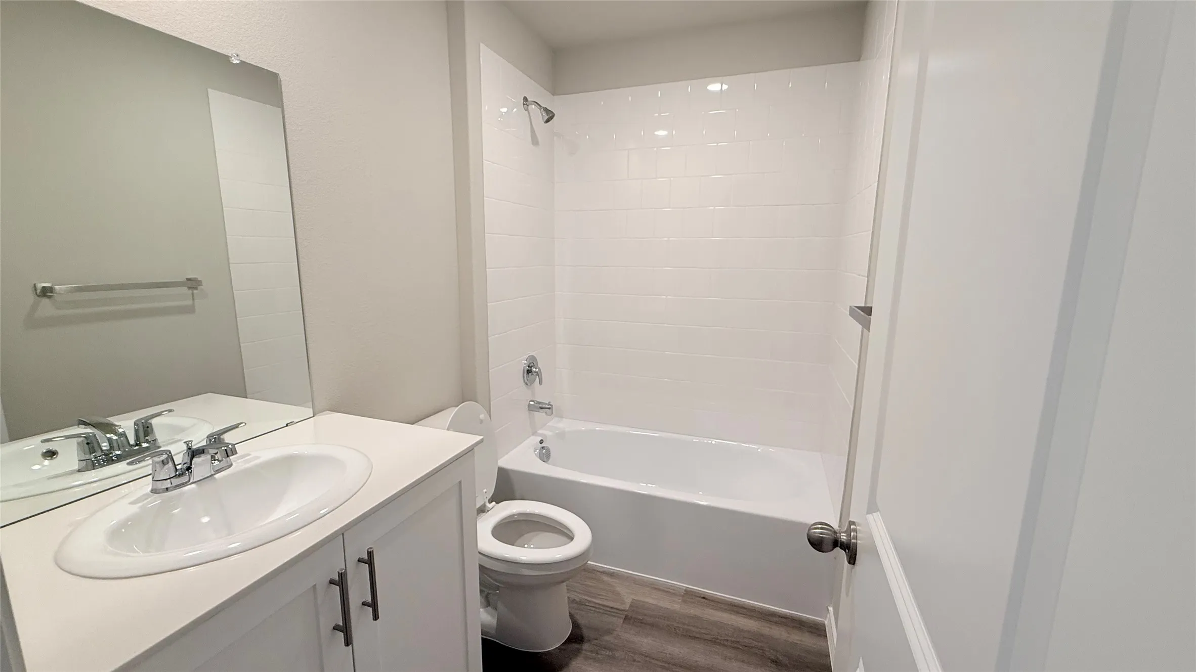 White vanity with an integrated sink, polished chrome faucet, full-width wall mirror, and a white subway tile shower surround