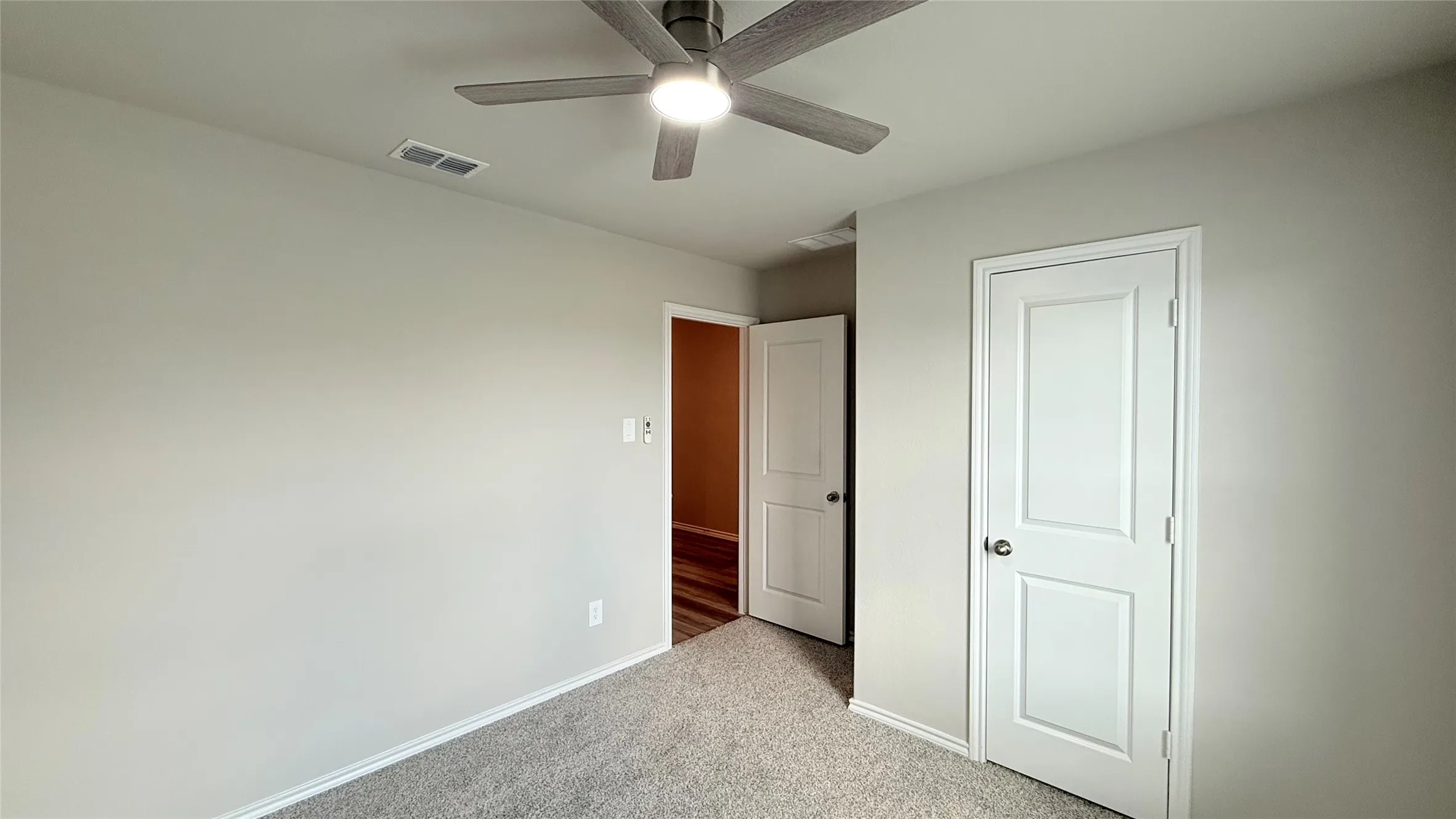 Neutral-toned walls, gray-toned carpet flooring, white paneled door, and a ceiling fan with integrated lighting