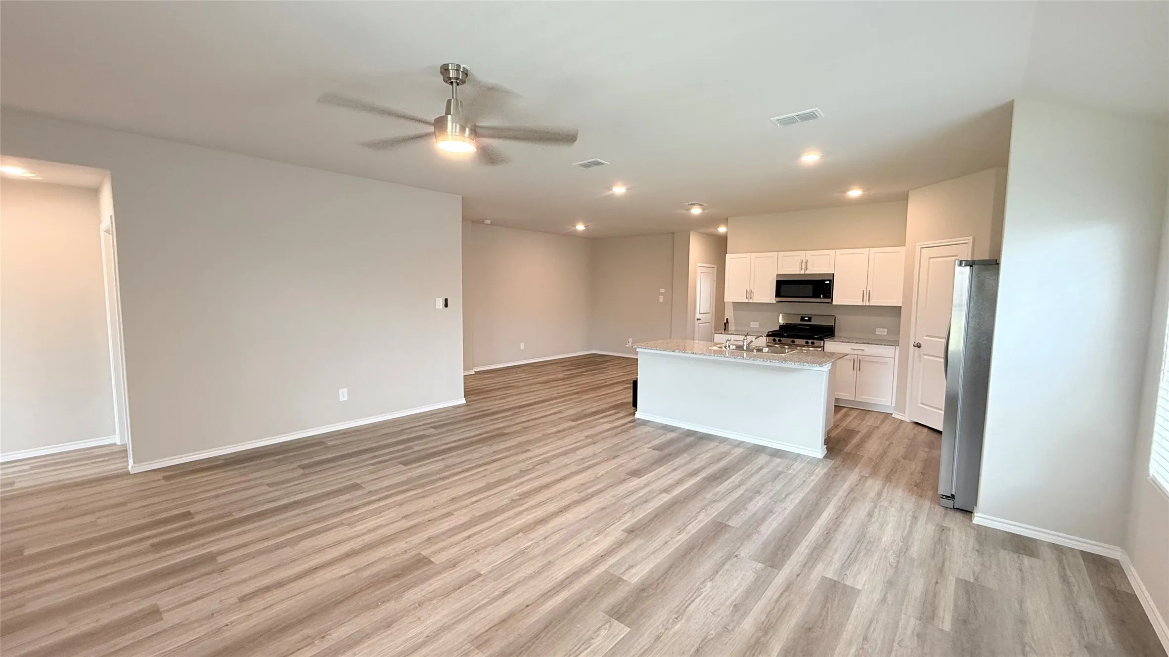 Expansive open-concept living area with wood-finish flooring, recessed lighting, and a ceiling fan
