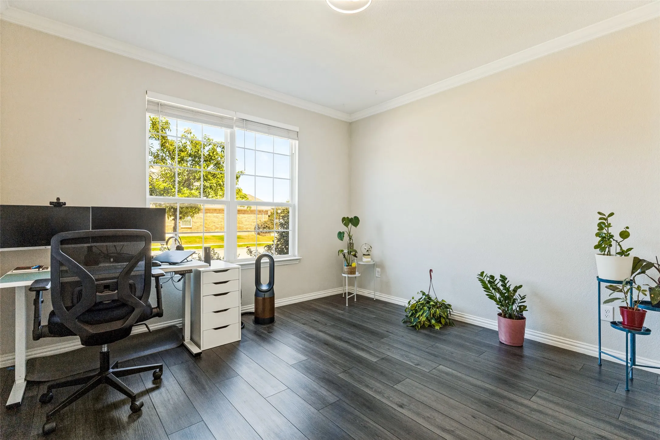 Light-filled room featuring durable wood-finish flooring, a large window with multiple panes, and crown molding
