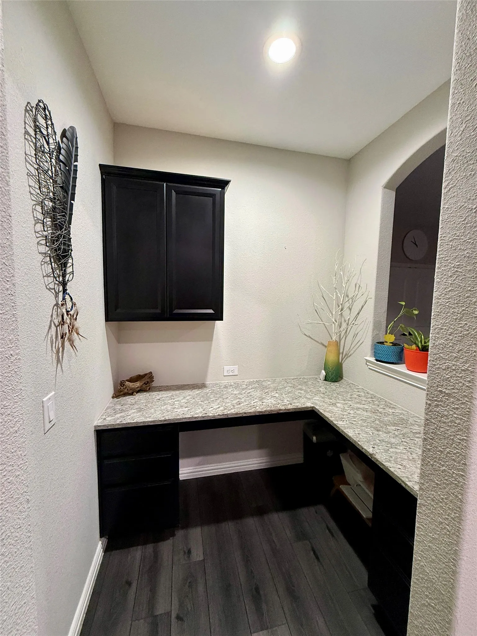 L-shaped built-in desk with dark cabinetry, light-toned countertop, and wood-finish flooring
