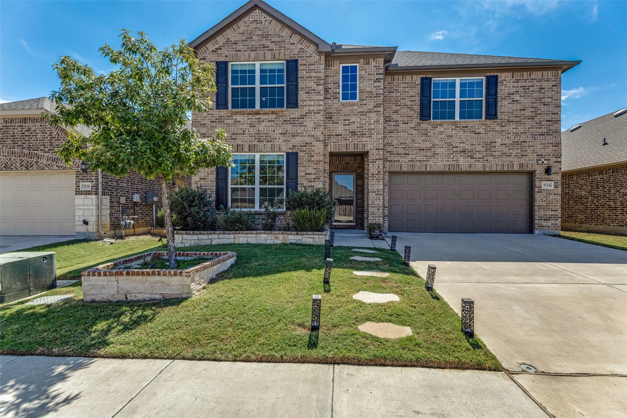Brick exterior with dark shutters, attached two-car garage, concrete driveway, and front lawn with stepping stones