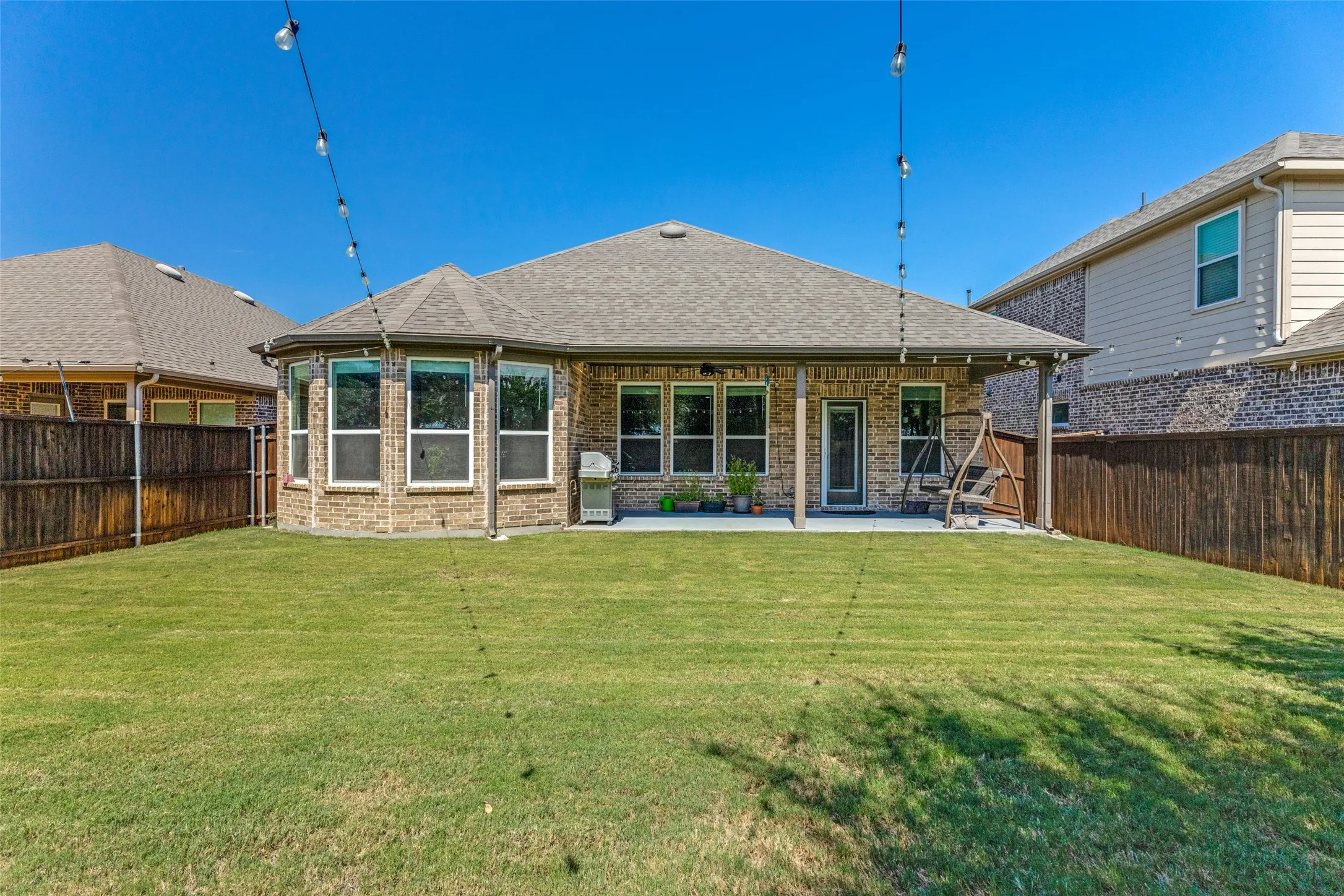 Expansive backyard with a manicured lawn, full privacy fencing, and a covered patio