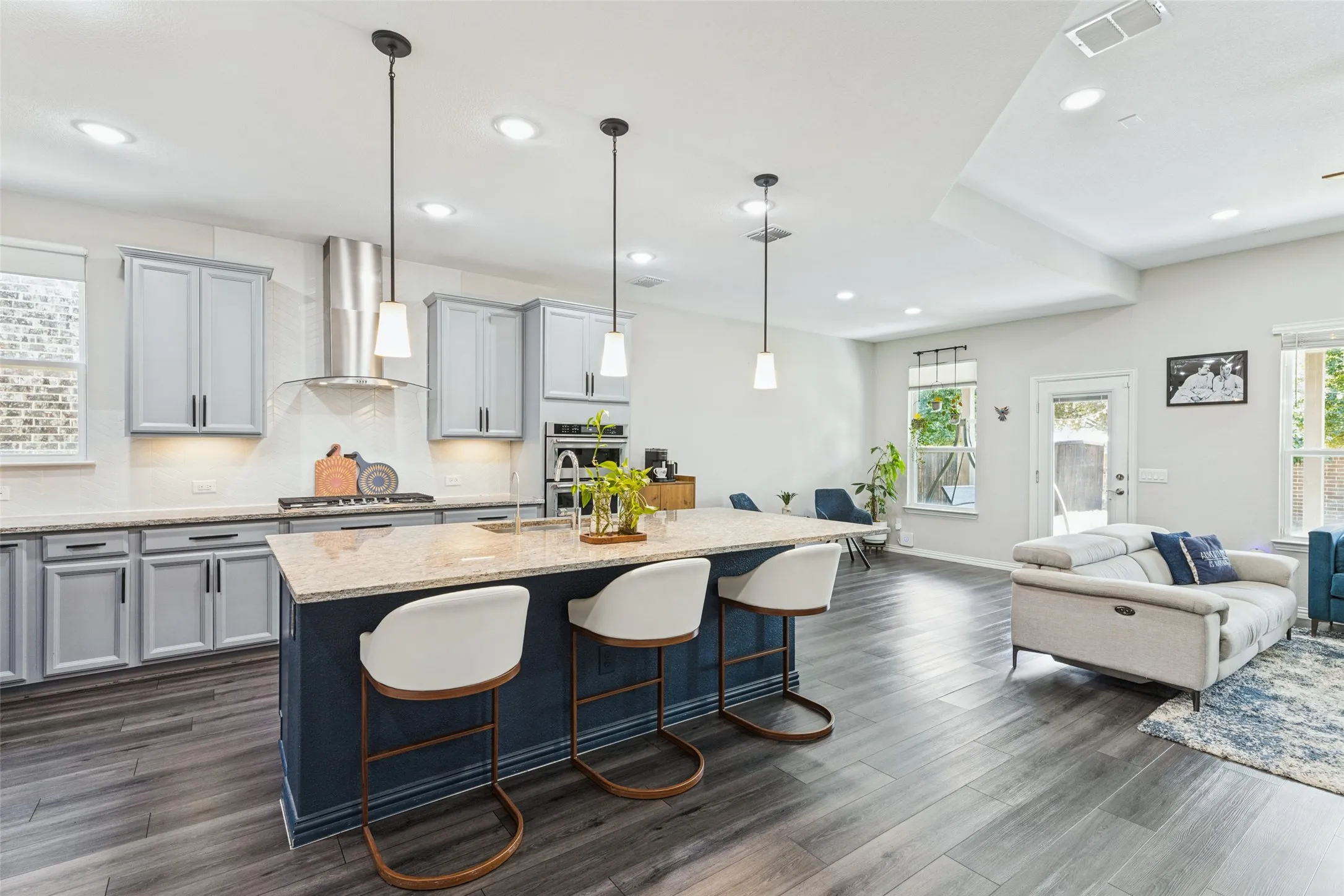 Spacious open-concept living area featuring wood-finish flooring, a kitchen island with seating, pendant lighting, recessed lighting, and light gray cabinetry