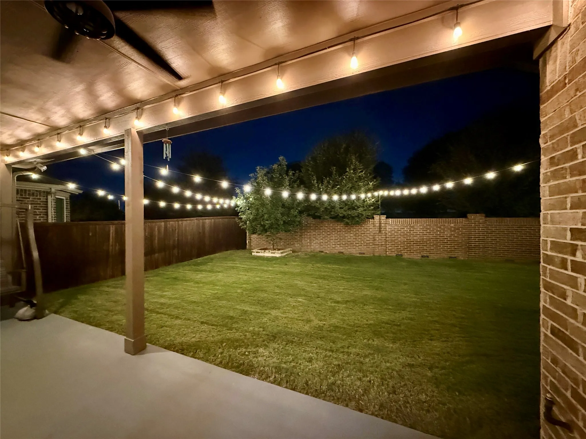 Covered patio with ceiling fan, string lighting, and direct access to a fenced backyard featuring a grassy lawn and brick perimeter wall