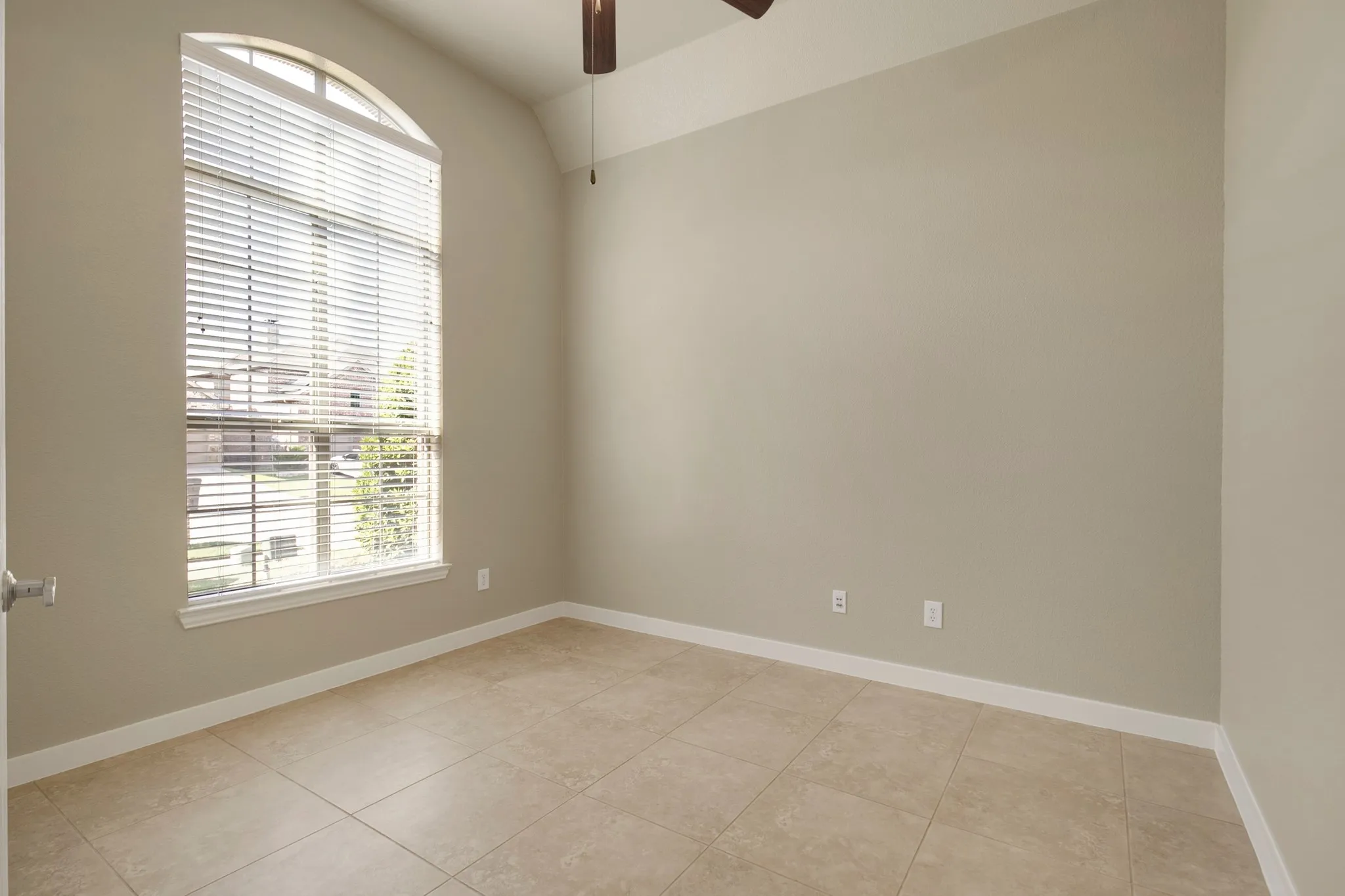 Arched window with blinds, tile flooring, neutral wall tones, and a ceiling fan