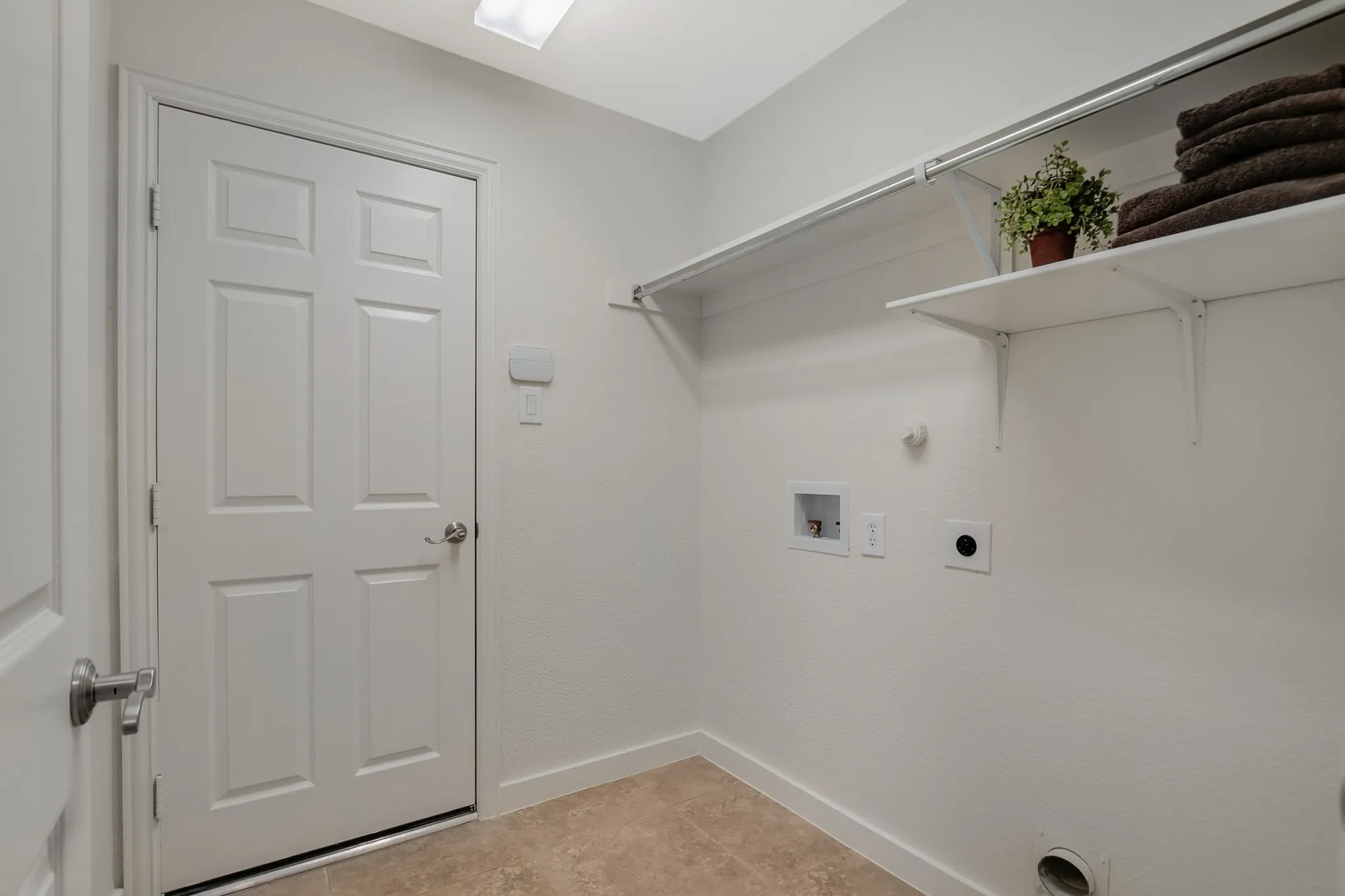 Laundry area with tiled flooring, white panel door, and built-in shelving with hanging rod