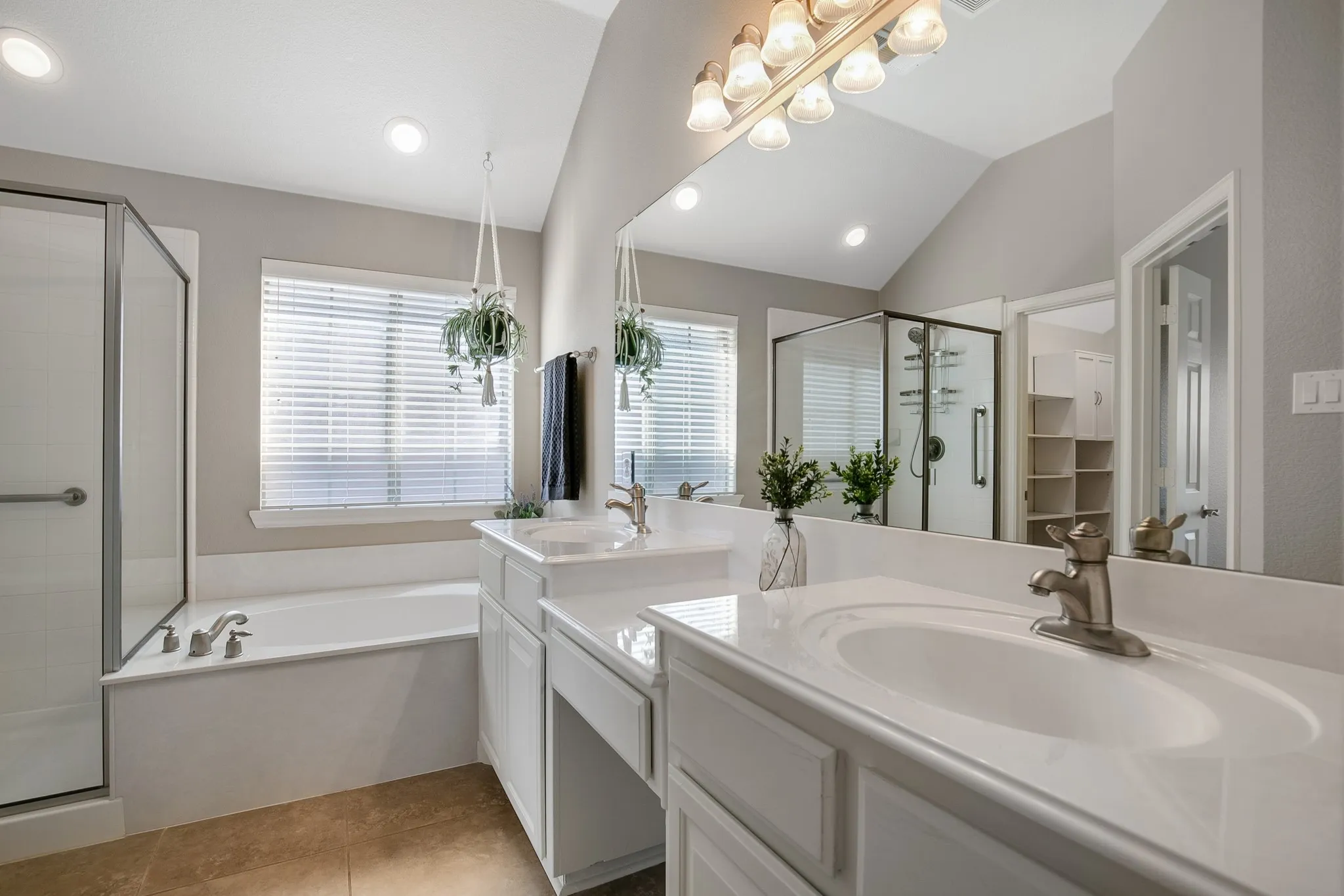 Dual vanity with undermount sinks and brushed nickel fixtures, separate enclosed shower with glass surround, built-in bathtub, and vaulted ceiling with recessed lighting