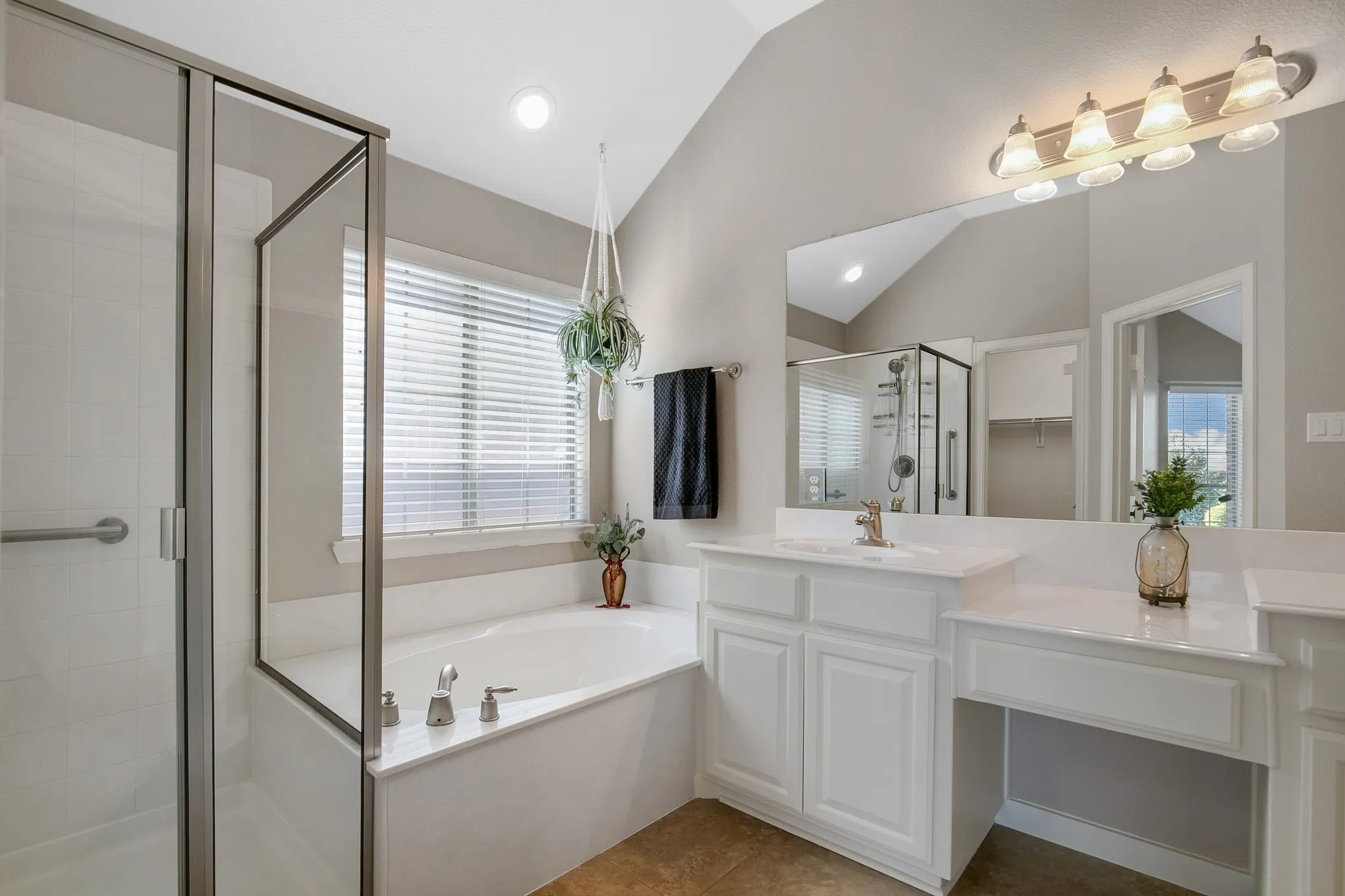 Vaulted ceiling with recessed lighting, glass-enclosed shower, built-in soaking tub, white vanity cabinetry with integrated sink, and extended countertop space
