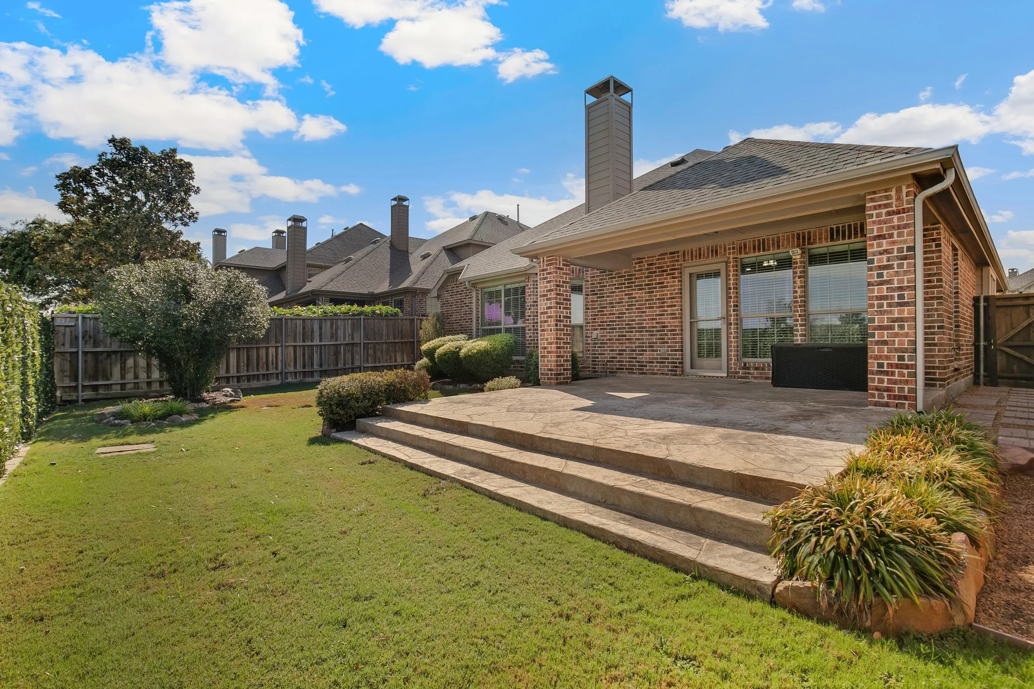 Brick exterior with a covered patio, extensive concrete patio, and a grassed yard