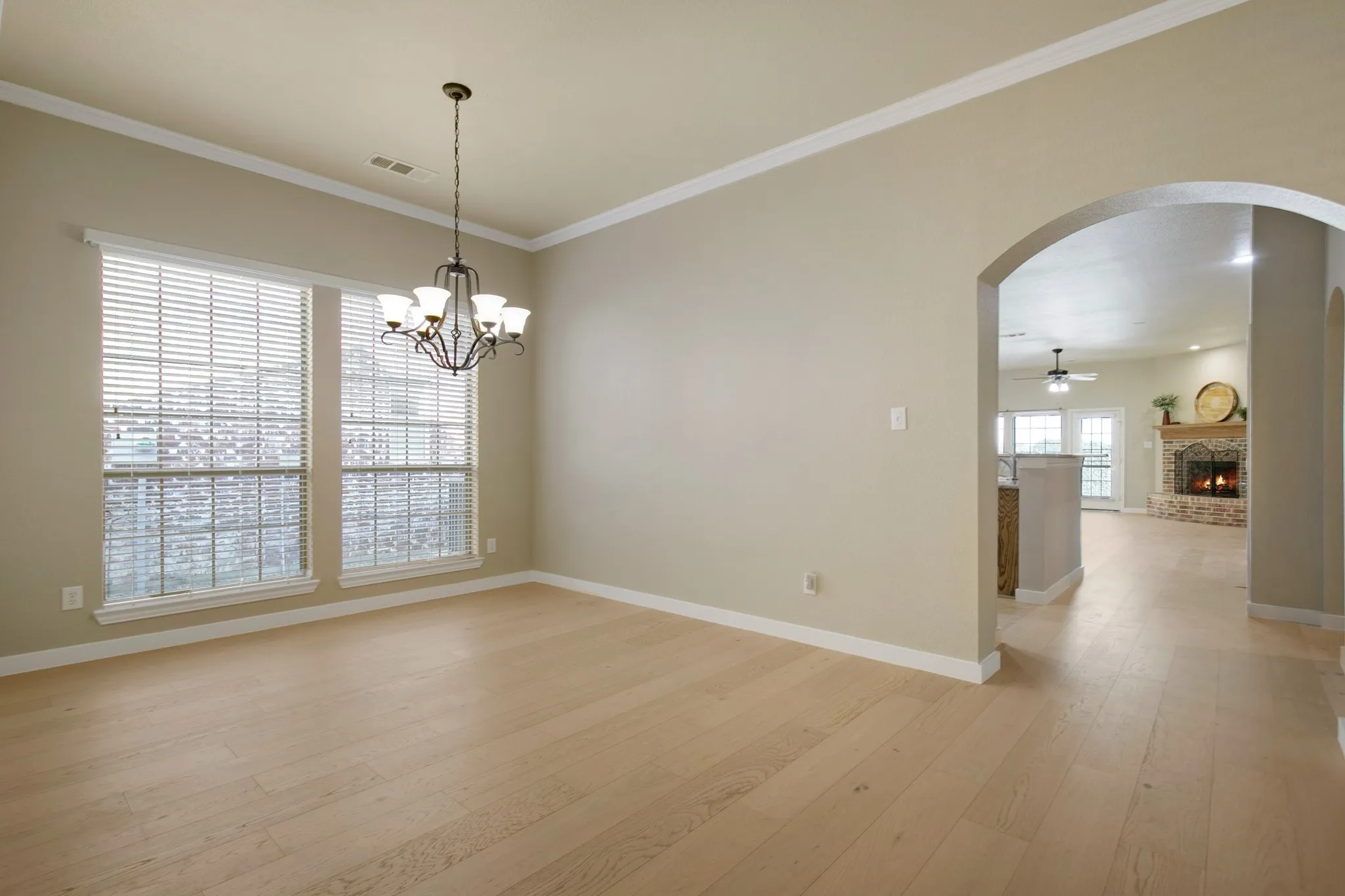 Natural light wood-finish flooring, two large windows, arched entryway, and a five-light chandelier