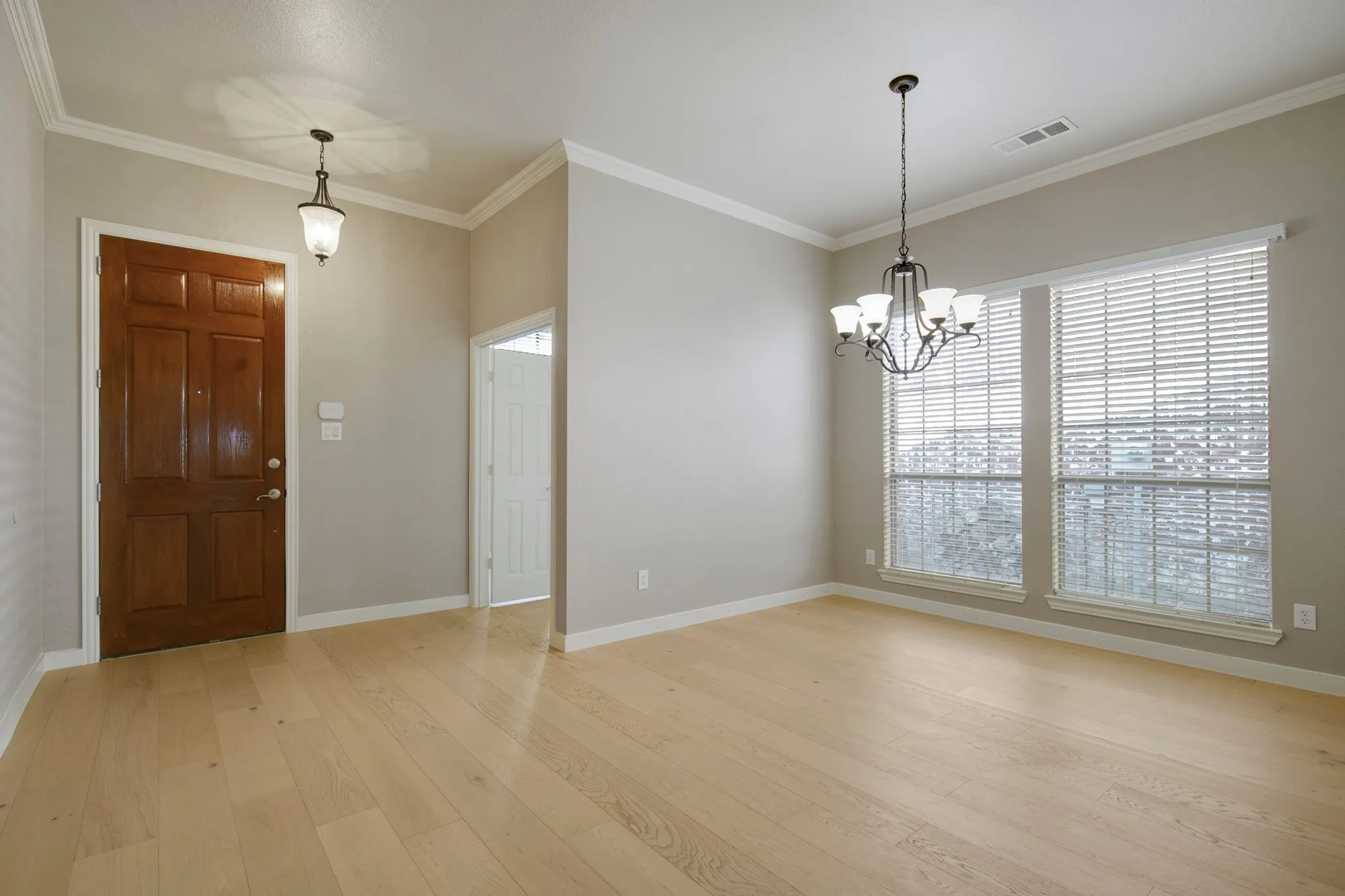 Hardwood-finish flooring throughout, two large windows with blinds, a five-light chandelier, a solid wood entry door, and crown molding