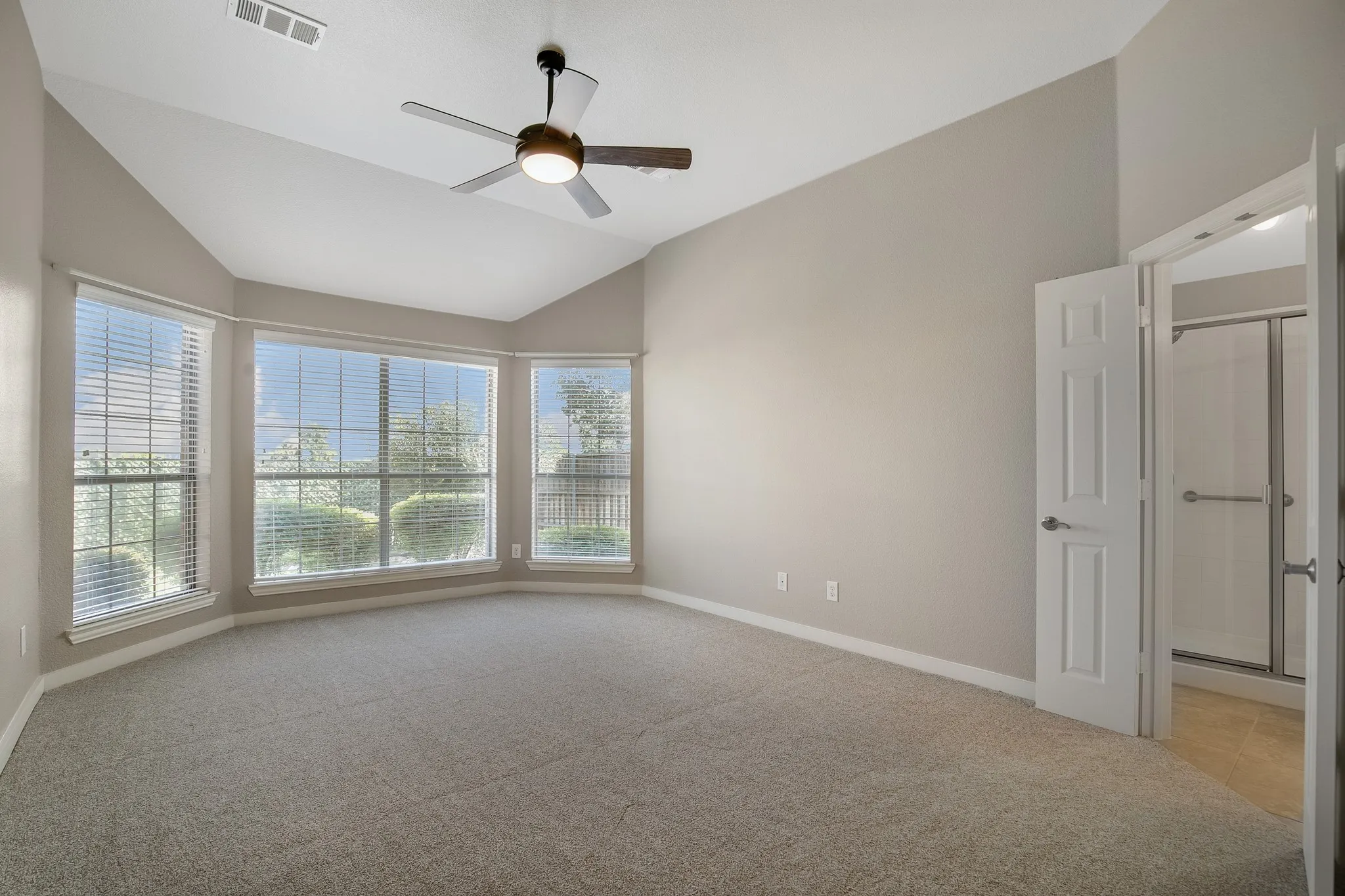Vaulted ceiling with an attached ceiling fan, bay window with blinds, carpeted flooring, and a shower enclosure