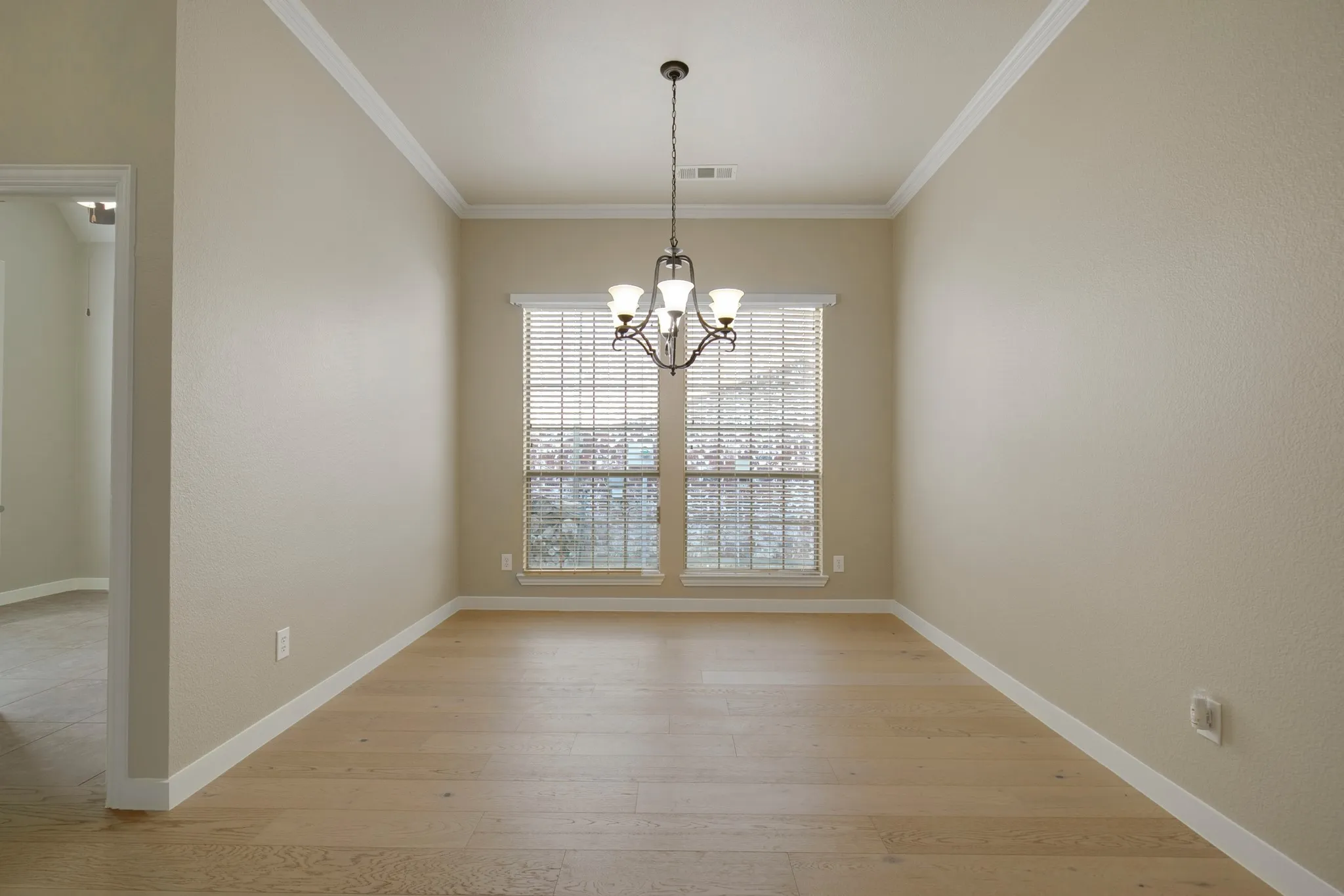 Wood-finish flooring, crown molding, and a chandelier illuminate this distinct area