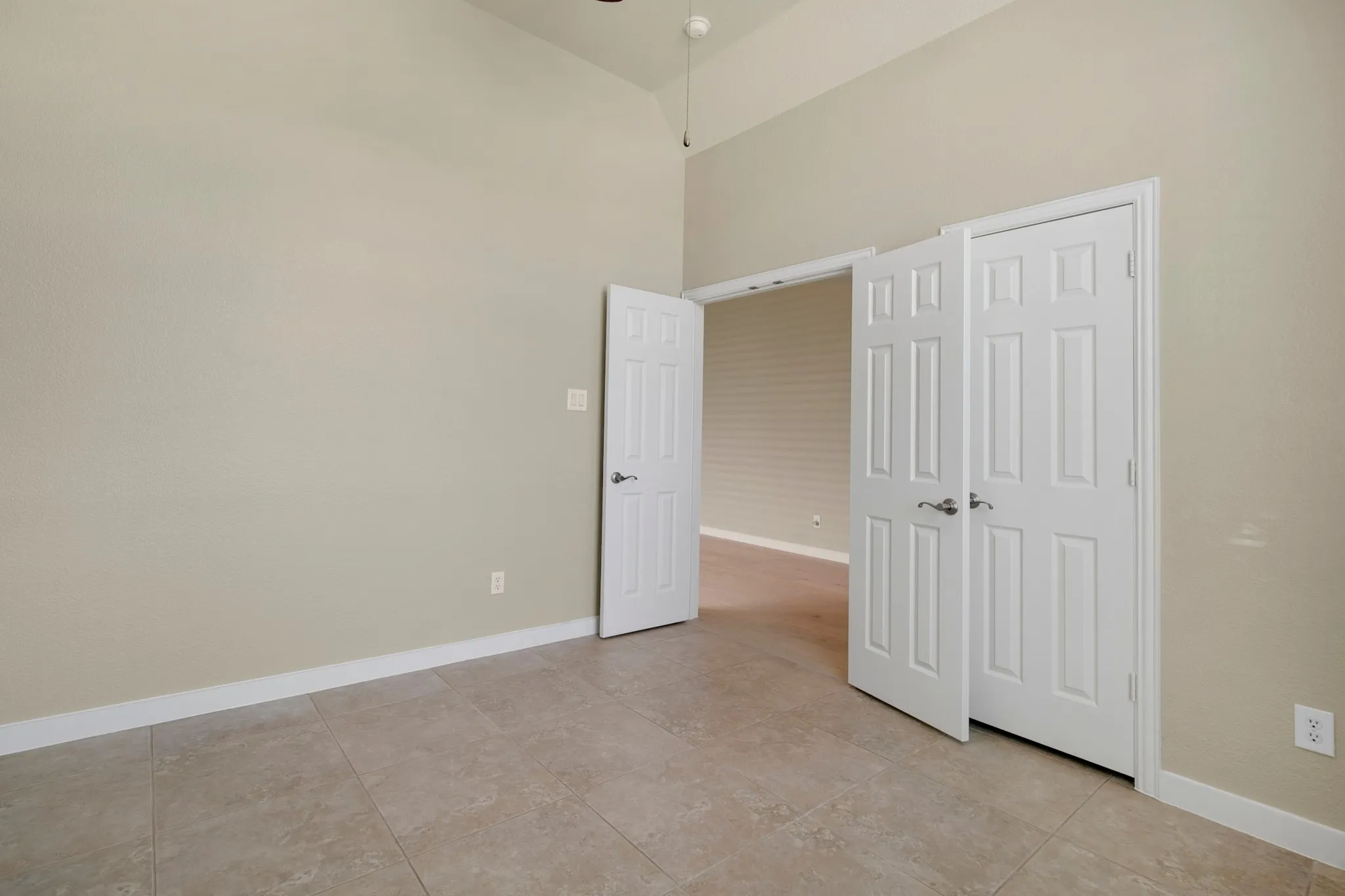 Vaulted ceiling with a ceiling fan, neutral wall color, and tile flooring