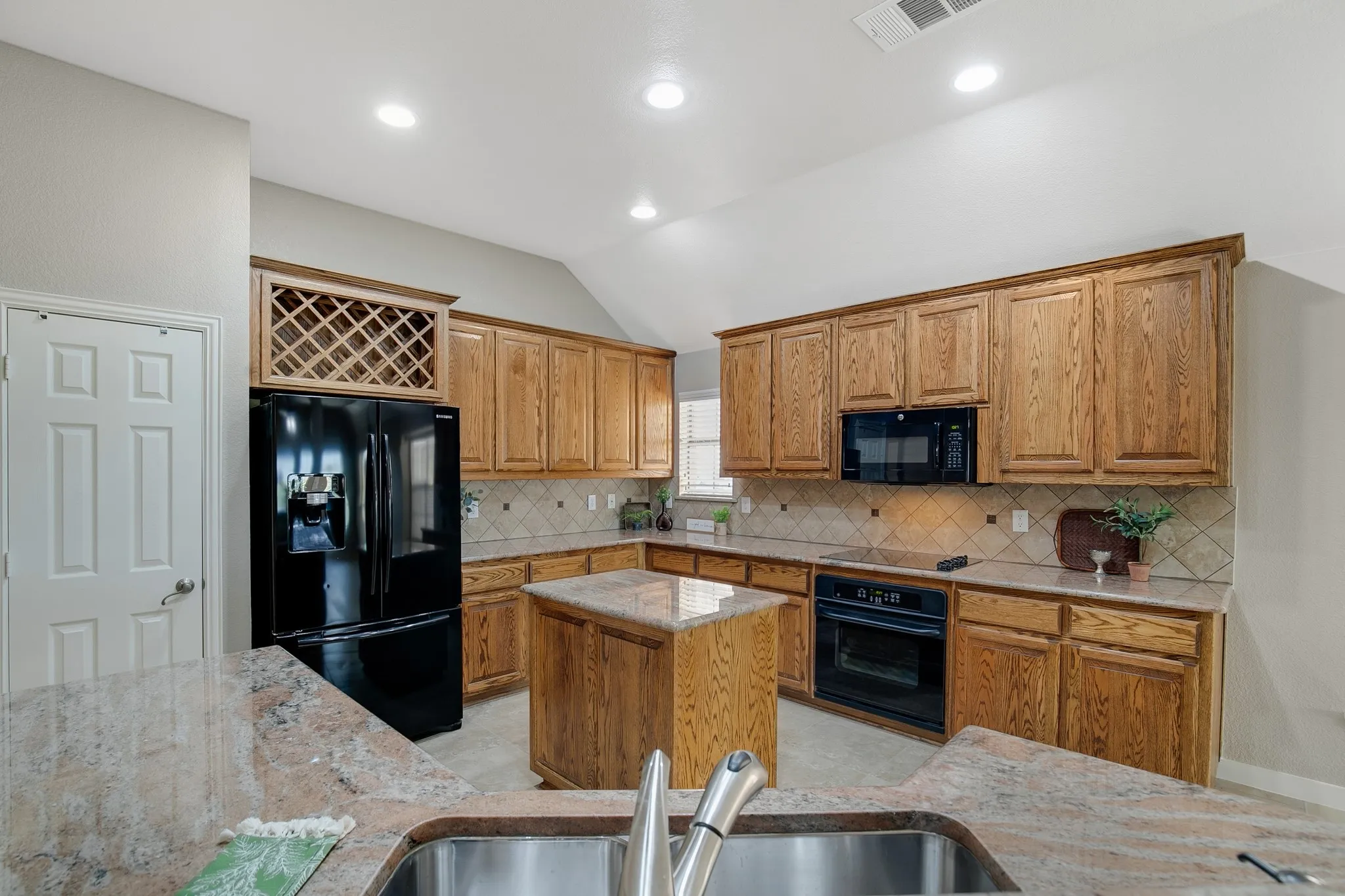 Kitchen featuring wood cabinetry, an integrated wine rack, black appliances, a central island, and stone countertops