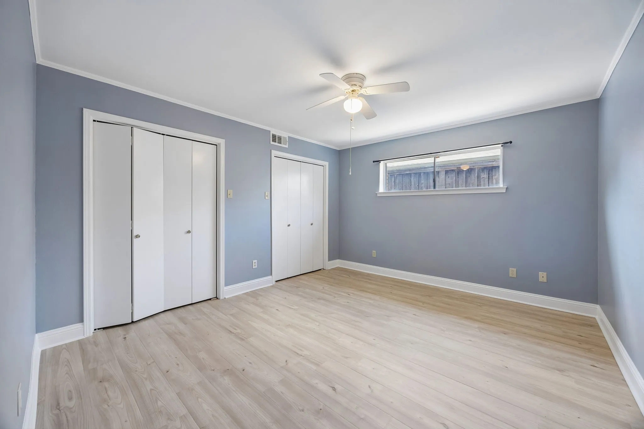 Spacious secondary bedroom with two closets, wood-look flooring, and a ceiling fan.