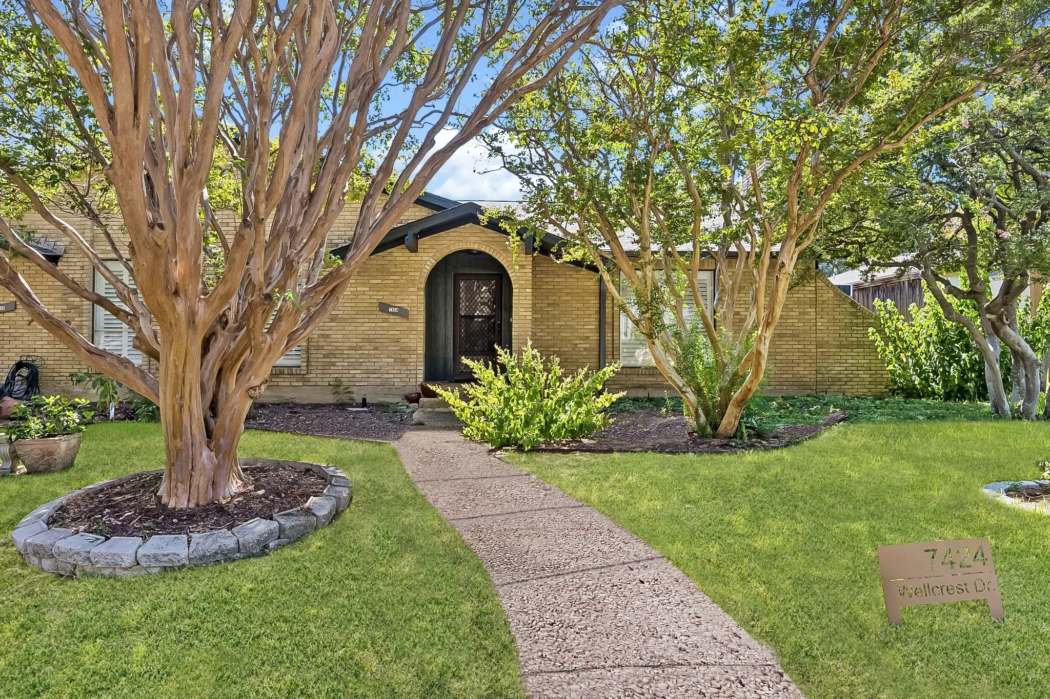 Inviting exterior framed by mature trees, with a charming arched entry and beautifully landscaped front yard.