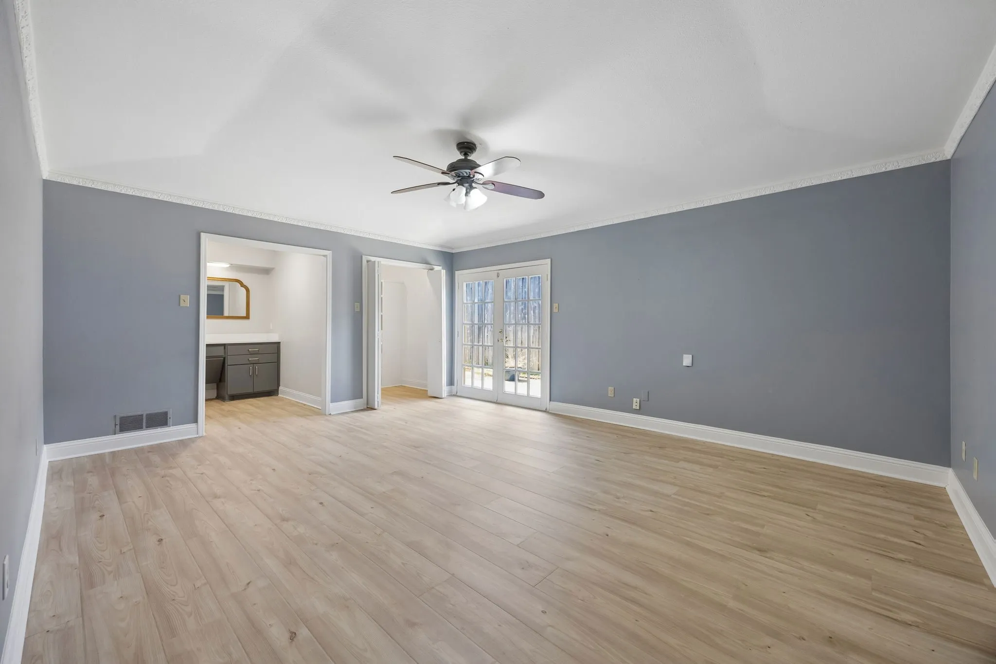 Spacious primary suite with wood-look flooring, French doors to the backyard, and a private en suite bath.