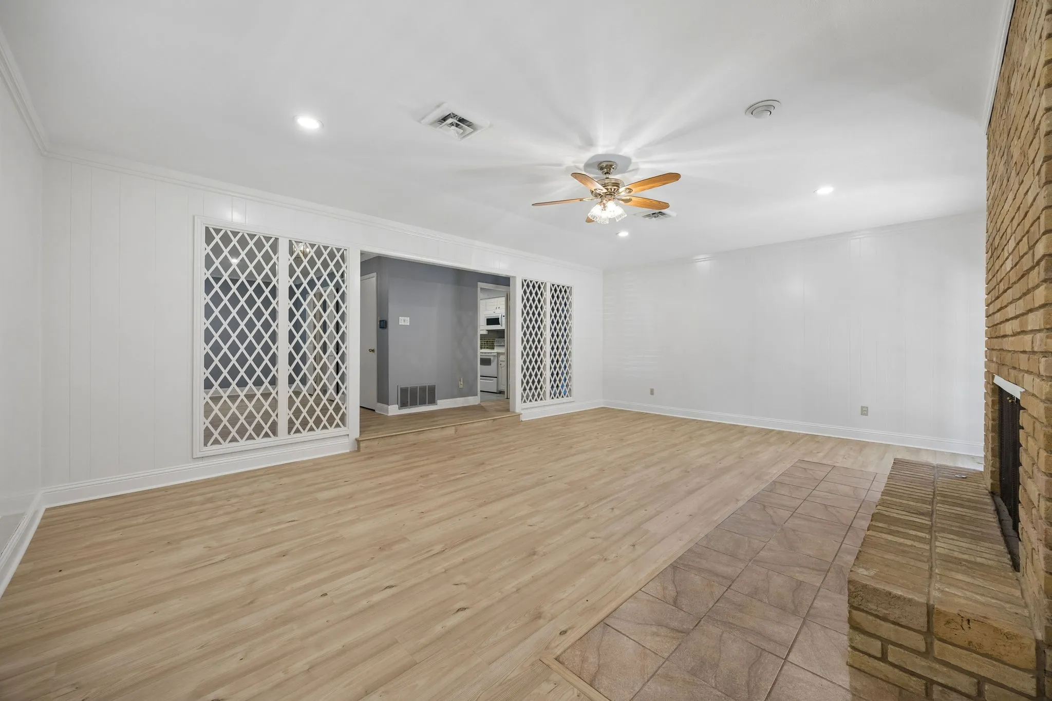 Another view of the living room highlights the brick fireplace and the open connection to both the kitchen and dining room through decorative latticework.