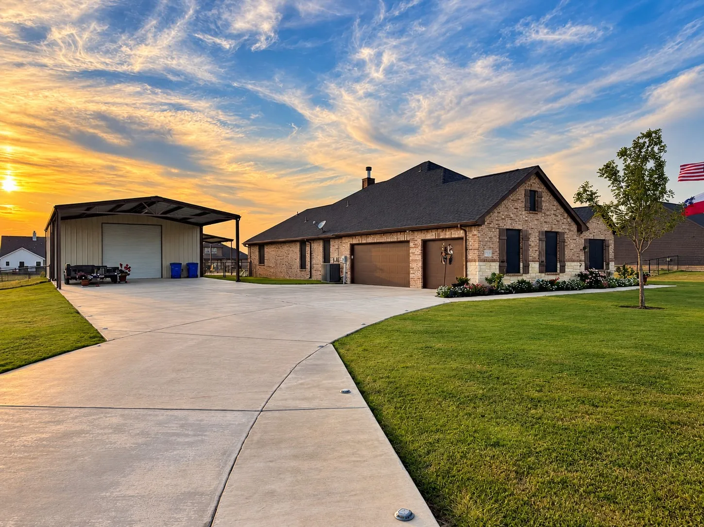 Brick exterior with stone accents, dark-shingle roof, brown garage doors, and a detached metal carport with a roll-up door