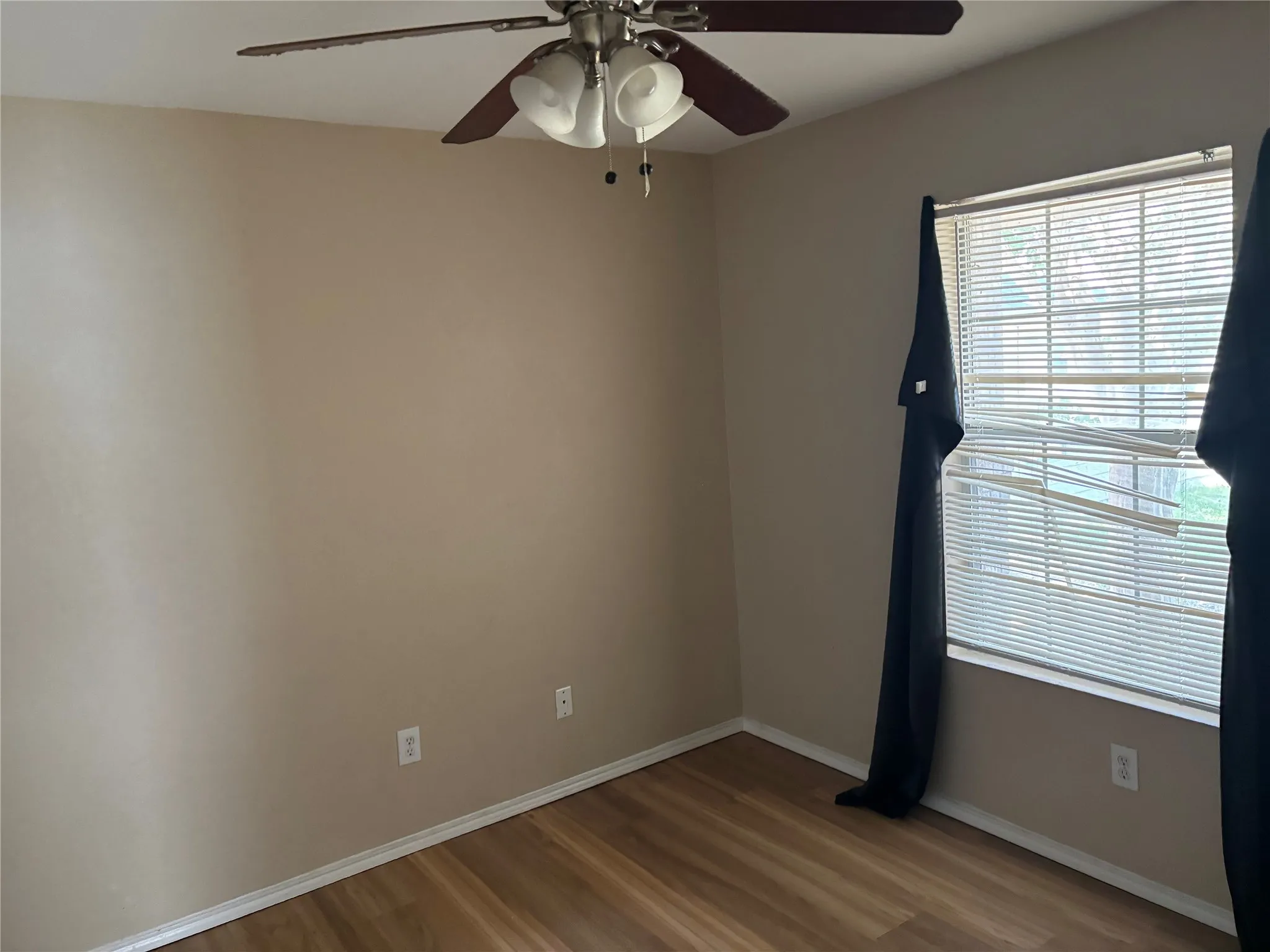 Room featuring wood-finish flooring, neutral wall tones, a ceiling fan with integrated lighting, and a window with blinds