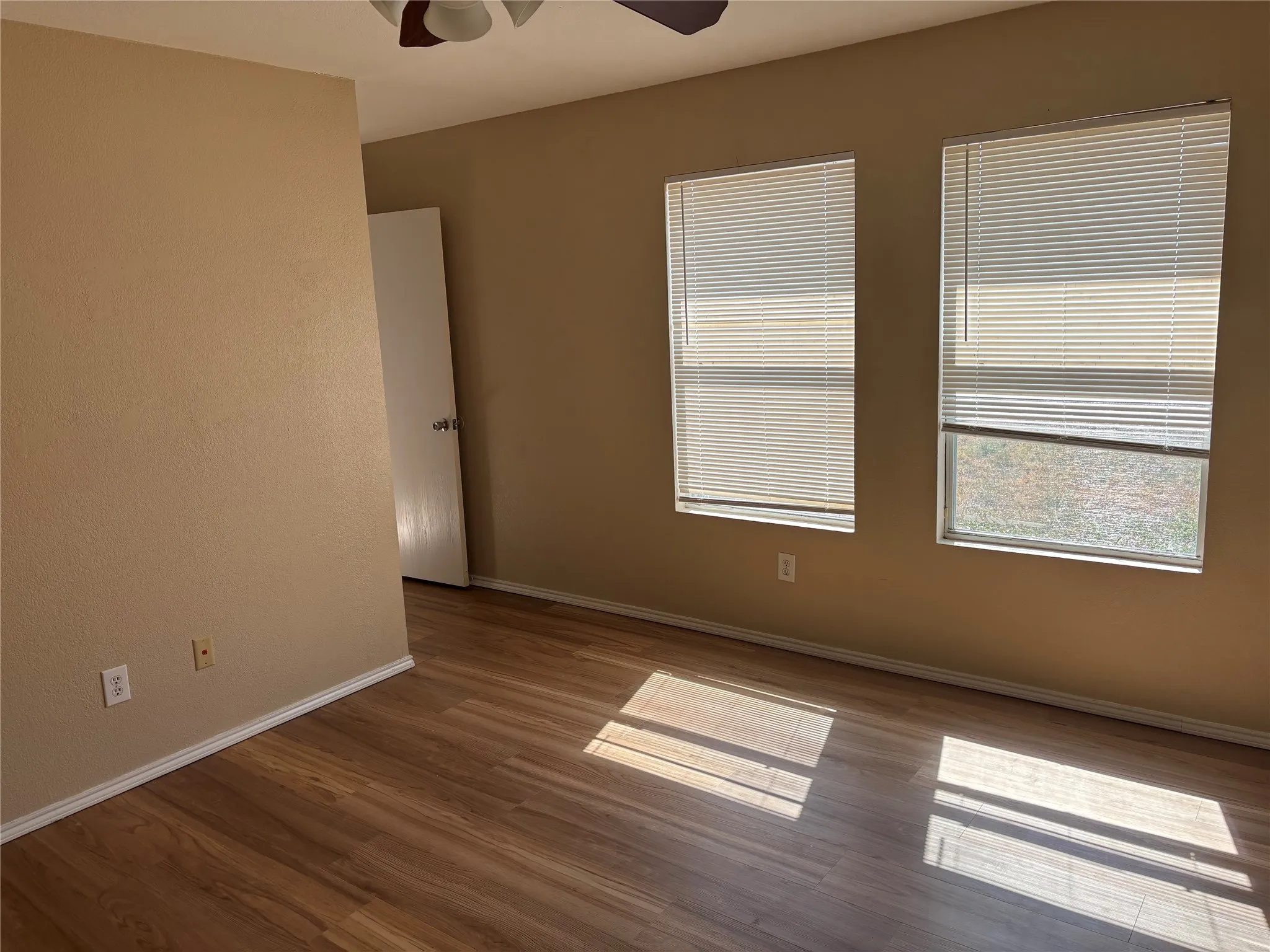 Wood-finish flooring, two windows with blinds, and neutral wall tones