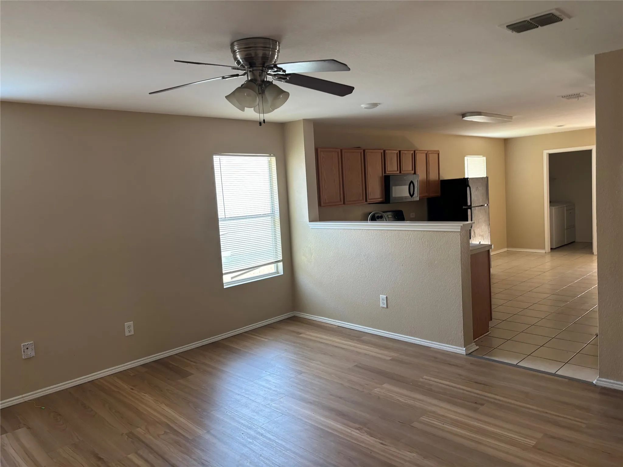 Wood-finish flooring throughout, ceiling fan with integrated lighting, kitchen featuring wood cabinetry, built-in microwave, and tile flooring