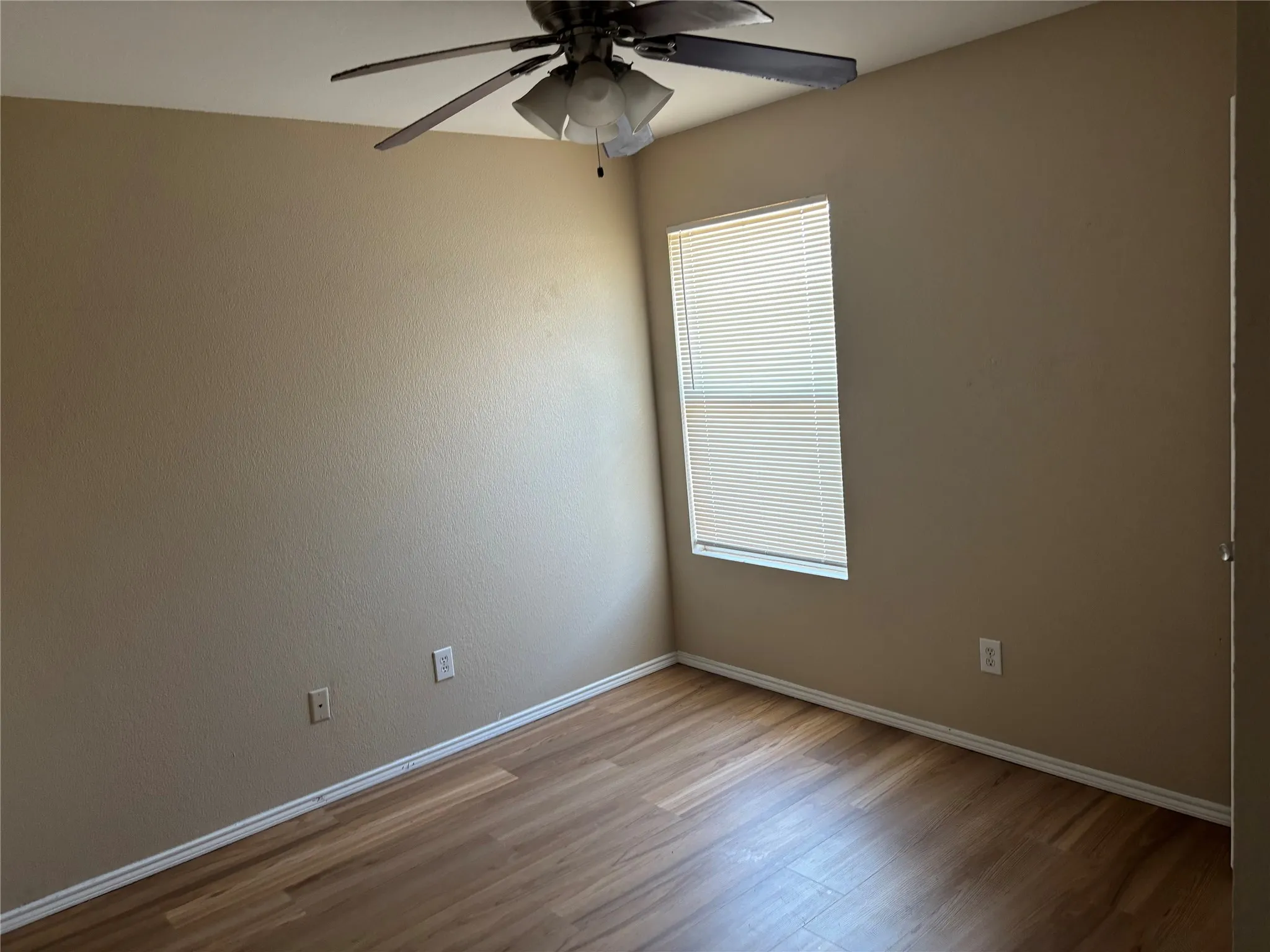 Wood-finish flooring with white trim, a single window with blinds, and a ceiling fan with integrated lighting