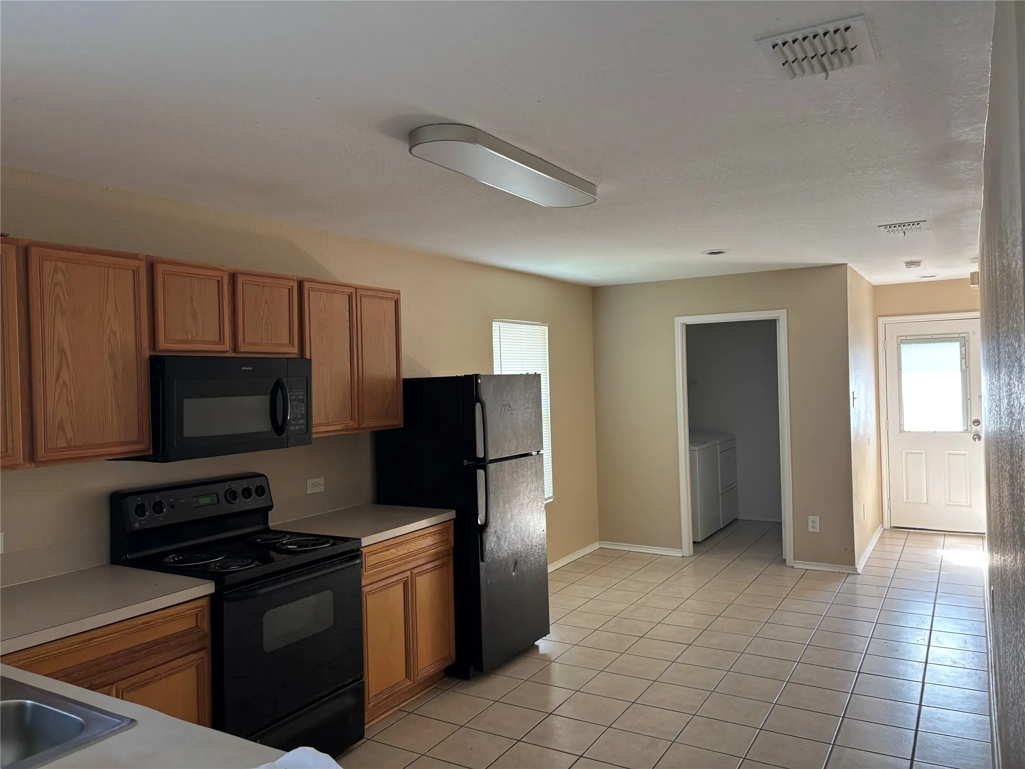 Kitchen featuring wood-finish cabinetry, black appliances, light-toned countertops, and tile flooring