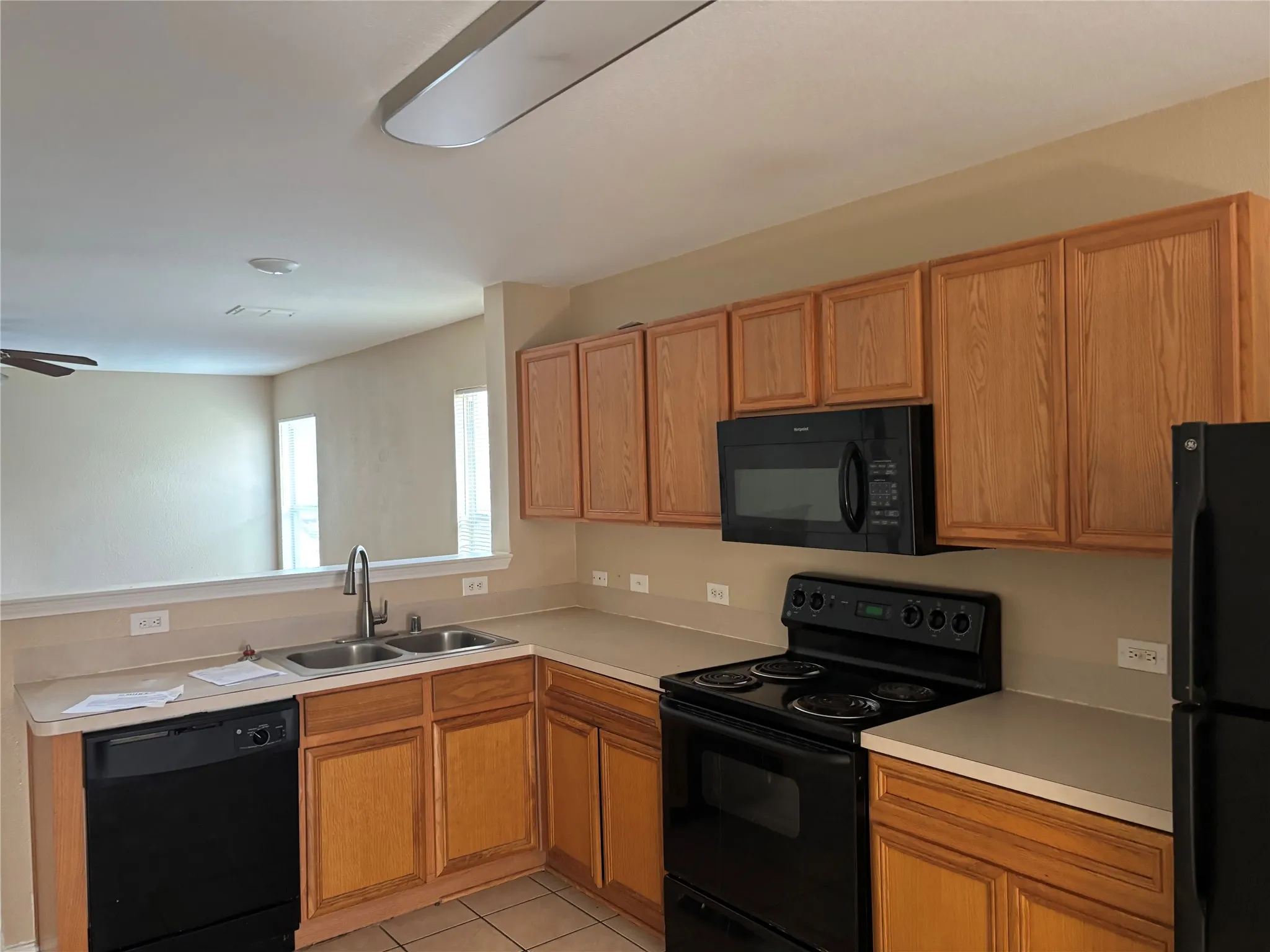 Kitchen featuring wood cabinetry, a double basin sink with a gooseneck faucet, black appliances, and neutral countertops