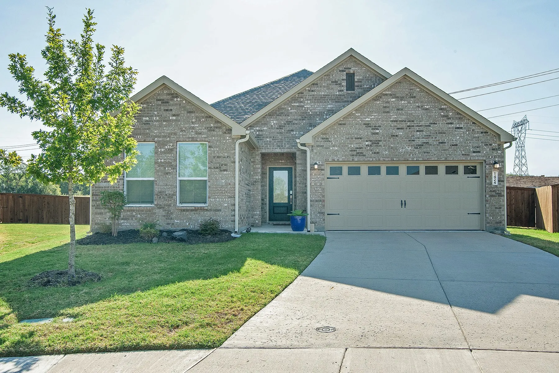 Brick exterior with a gabled roofline, two-car garage with window inserts, concrete driveway, and front lawn with a young tree