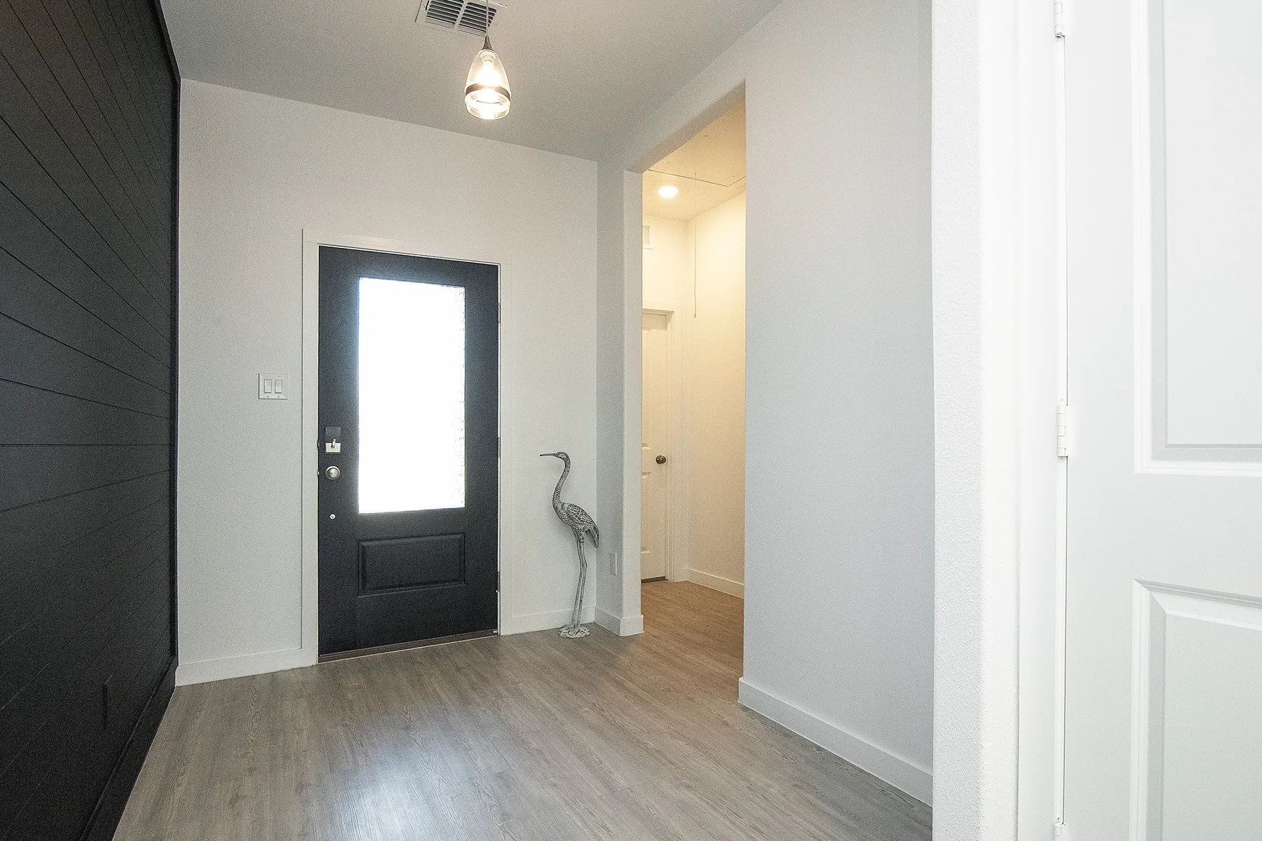 Entryway featuring wood-finish flooring, a black paneled accent wall, and a black entry door with an opaque glass insert