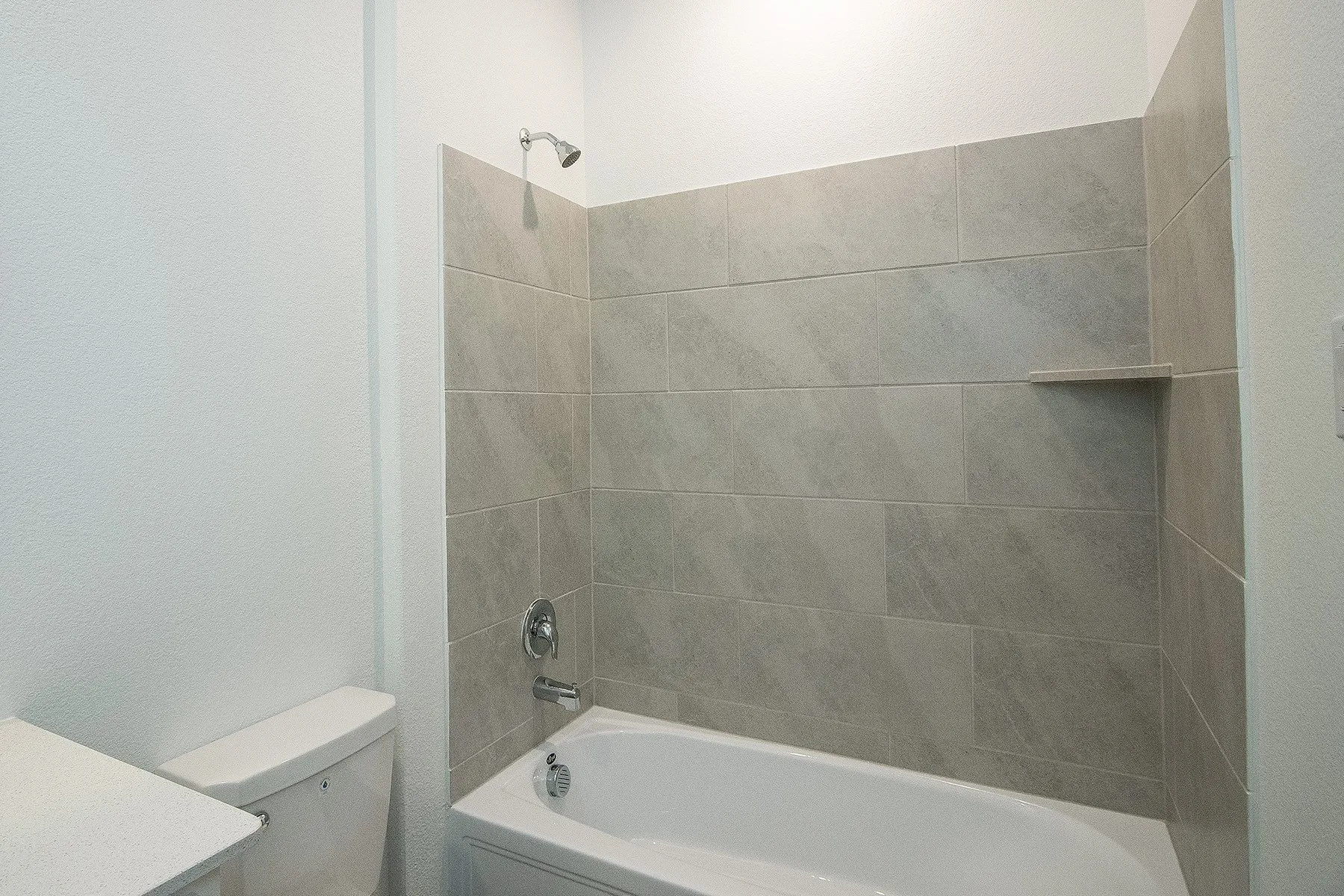 Tub-shower combination with light-toned rectangular wall tiles, built-in shower shelf, and chrome fixtures