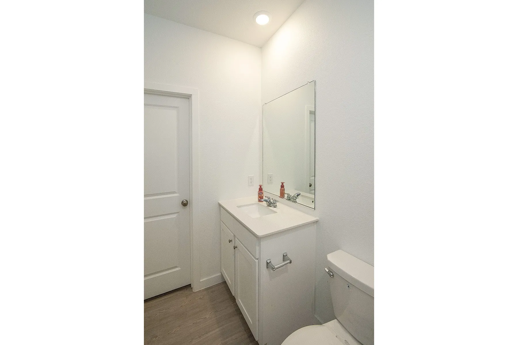 White vanity with integrated sink, rectangular mirror, and wood-finish flooring