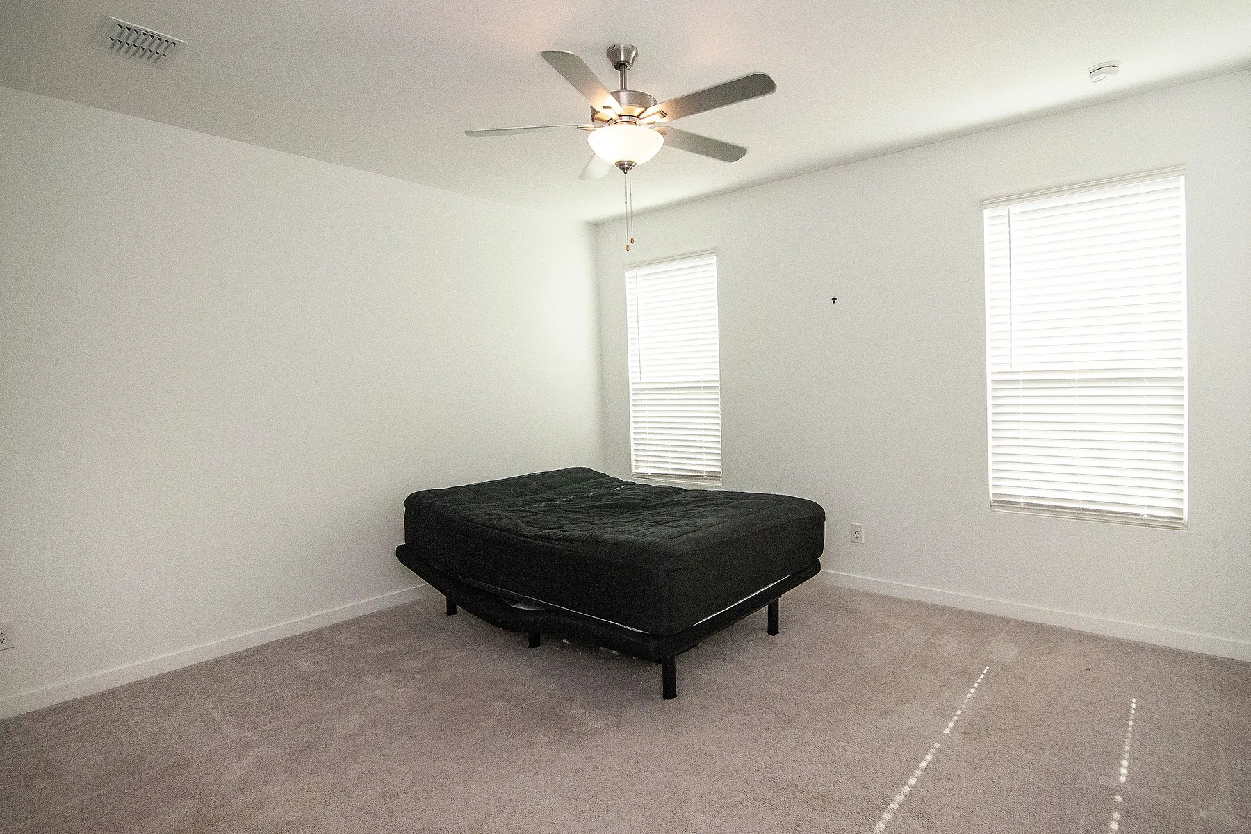 Carpeted flooring, two windows with blinds, ceiling fan with integrated lighting, and neutral wall tones