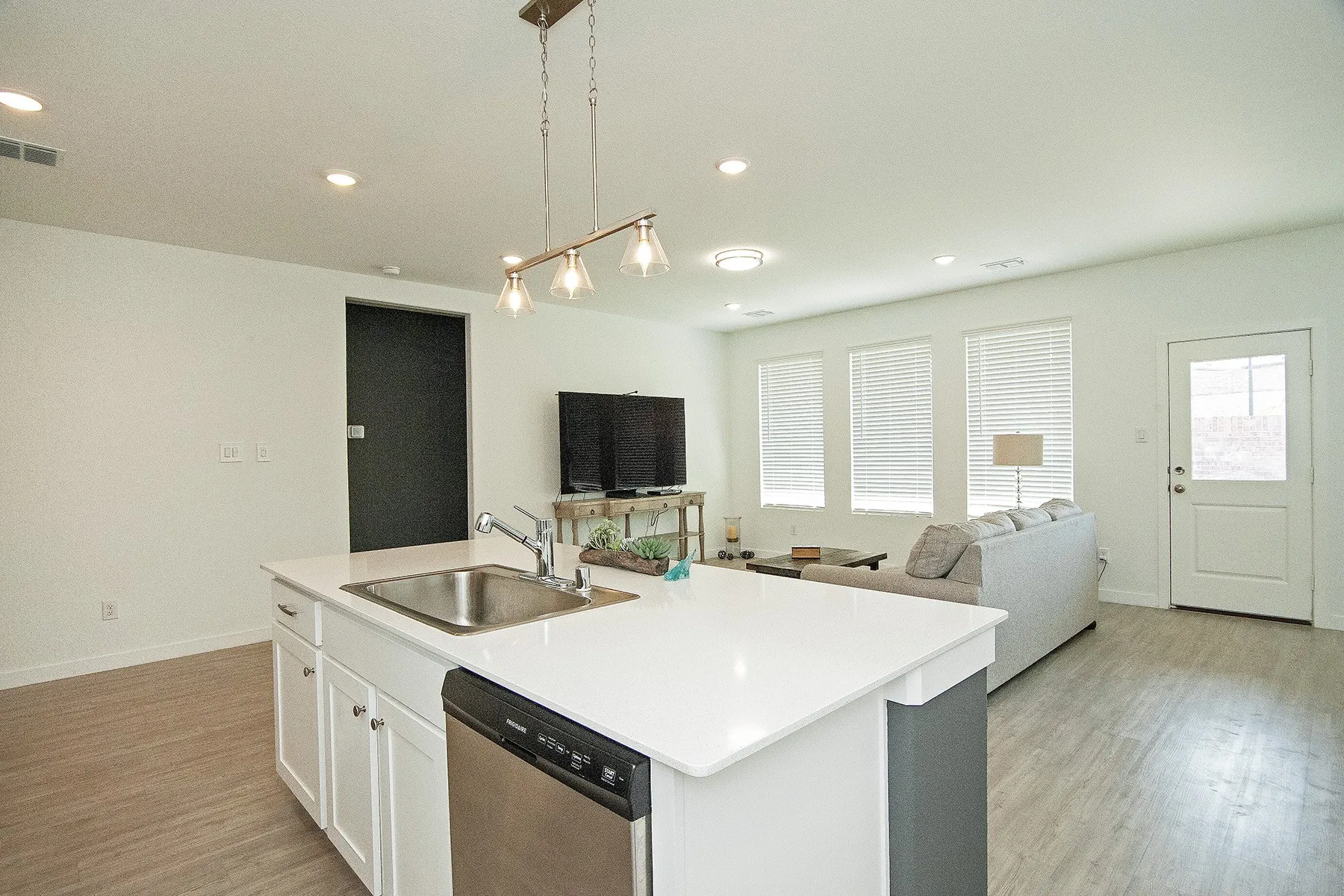 Kitchen island with integrated sink, white cabinetry, and stainless steel dishwasher