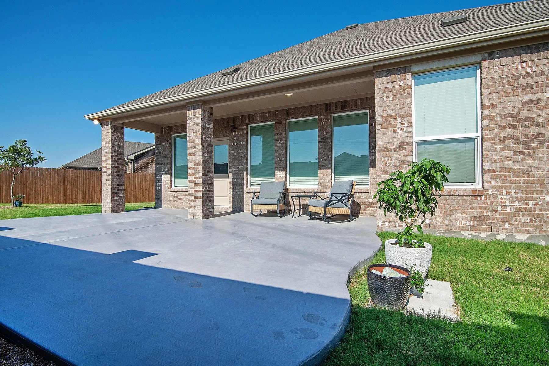 Expansive concrete patio with brick support pillars, covered patio area, and a lush green lawn