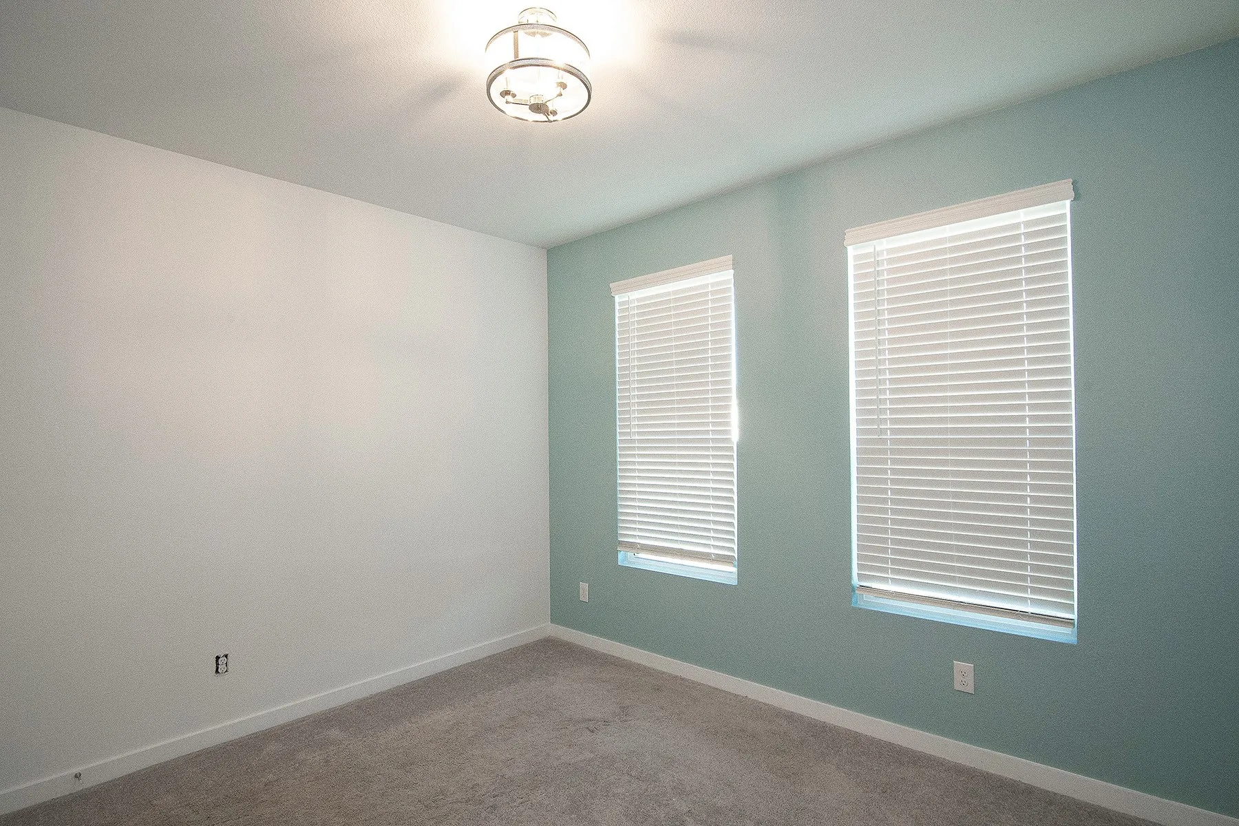 Neutral tone walls with an accent wall, two windows with blinds, and ceiling-mounted lighting