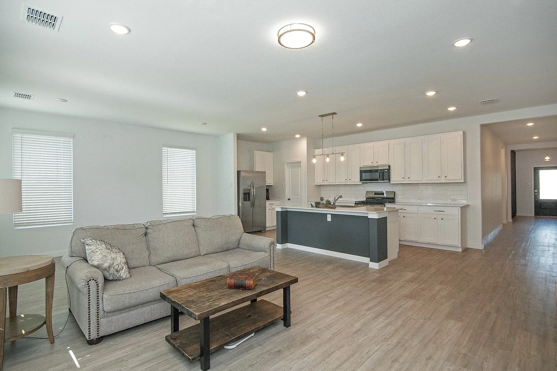 Recessed lighting, wood-finish flooring, white cabinetry, stainless steel appliances, and a kitchen island with pendant lighting