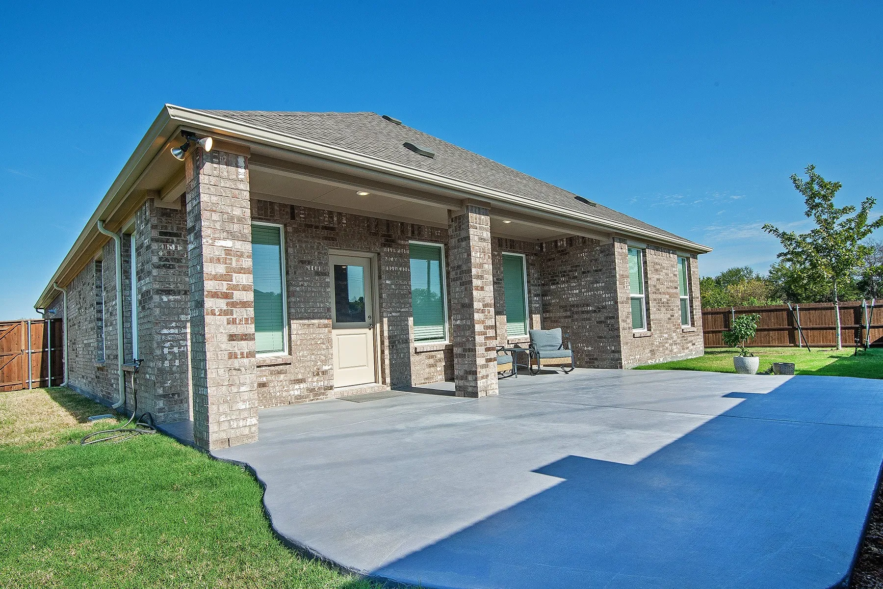 Brick exterior with a covered patio, expansive concrete hardscaping, and a fully fenced yard
