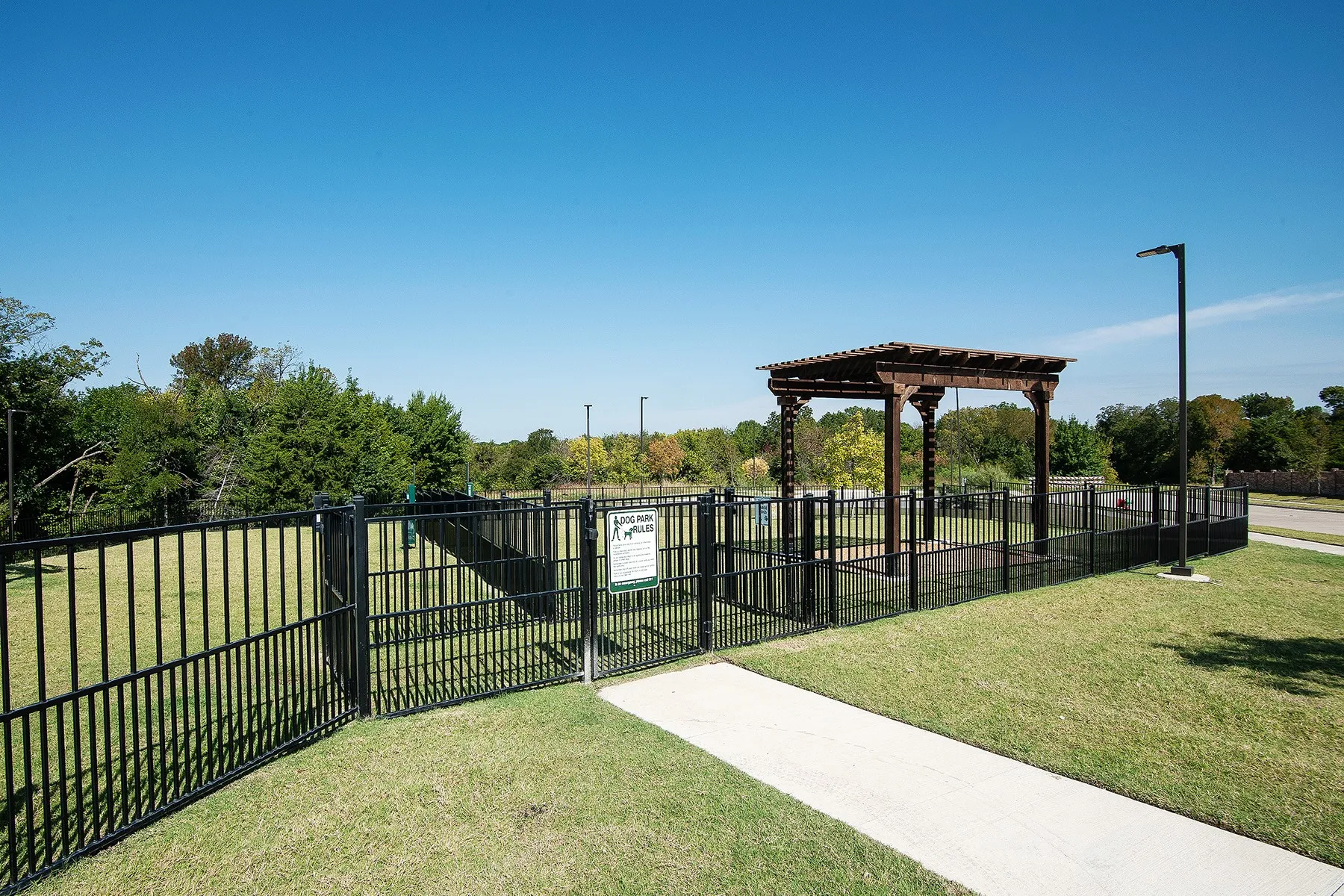 Fenced outdoor area featuring a pergola structure, concrete pathway, and manicured grass