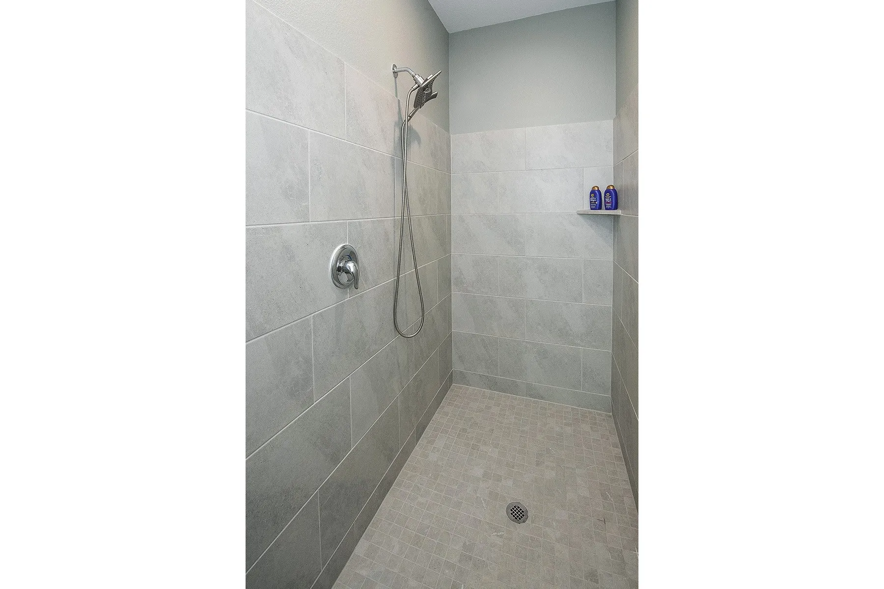 Tiled shower enclosure featuring a handheld showerhead, chrome fixtures, integrated wall niche, and mosaic tile flooring