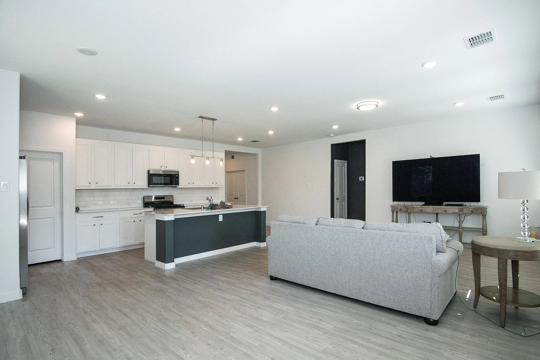 Open-concept living area with wood-finish flooring, recessed lighting, and a kitchen featuring white cabinetry, subway tile backsplash, and a central island with a pendant light fixture