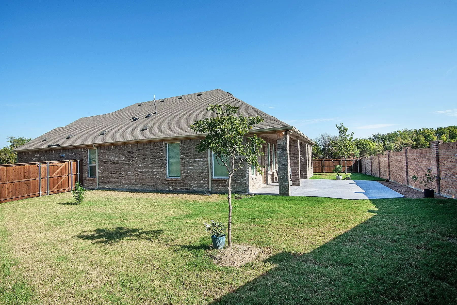 Brick exterior with a shingle roof, wood privacy fence, and an expansive concrete patio