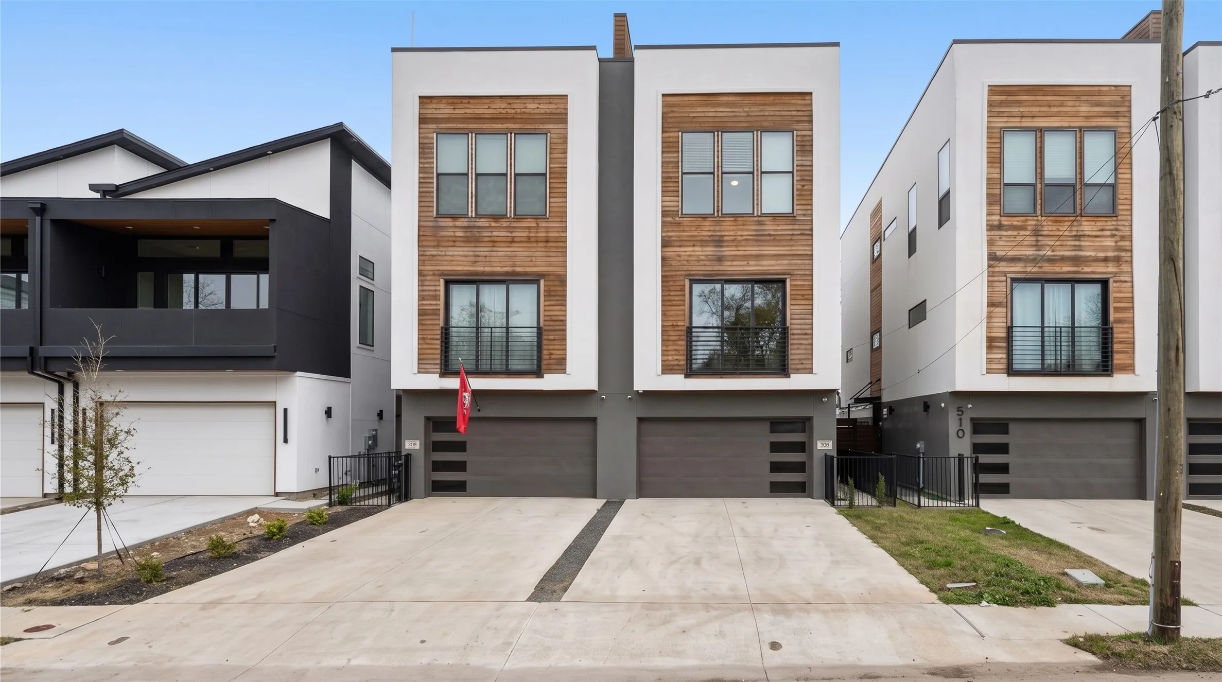 Contemporary exterior featuring white and wood-finish siding, multiple large windows, a two-car garage with horizontal paneling, and a concrete driveway